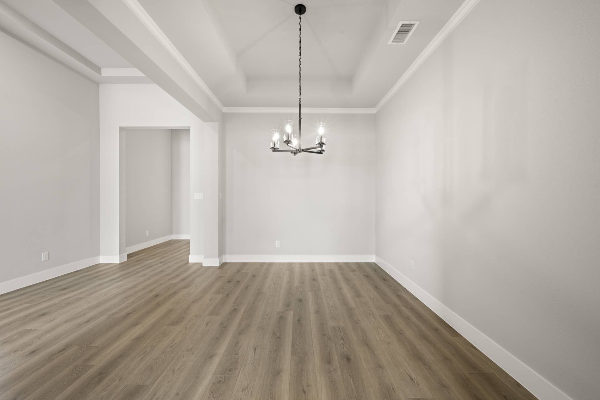 Spacious dining room with modern chandelier and hardwood flooring.