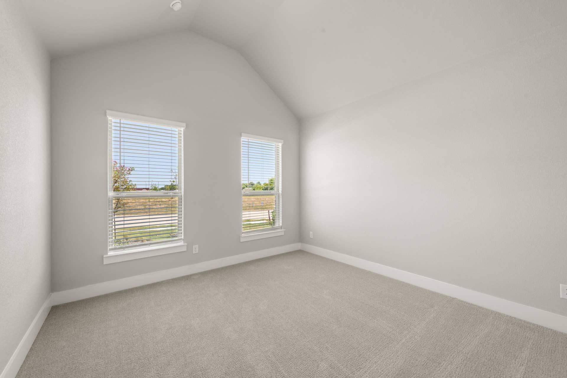 Bright bedroom interior with neutral walls, carpet, and two large windows.