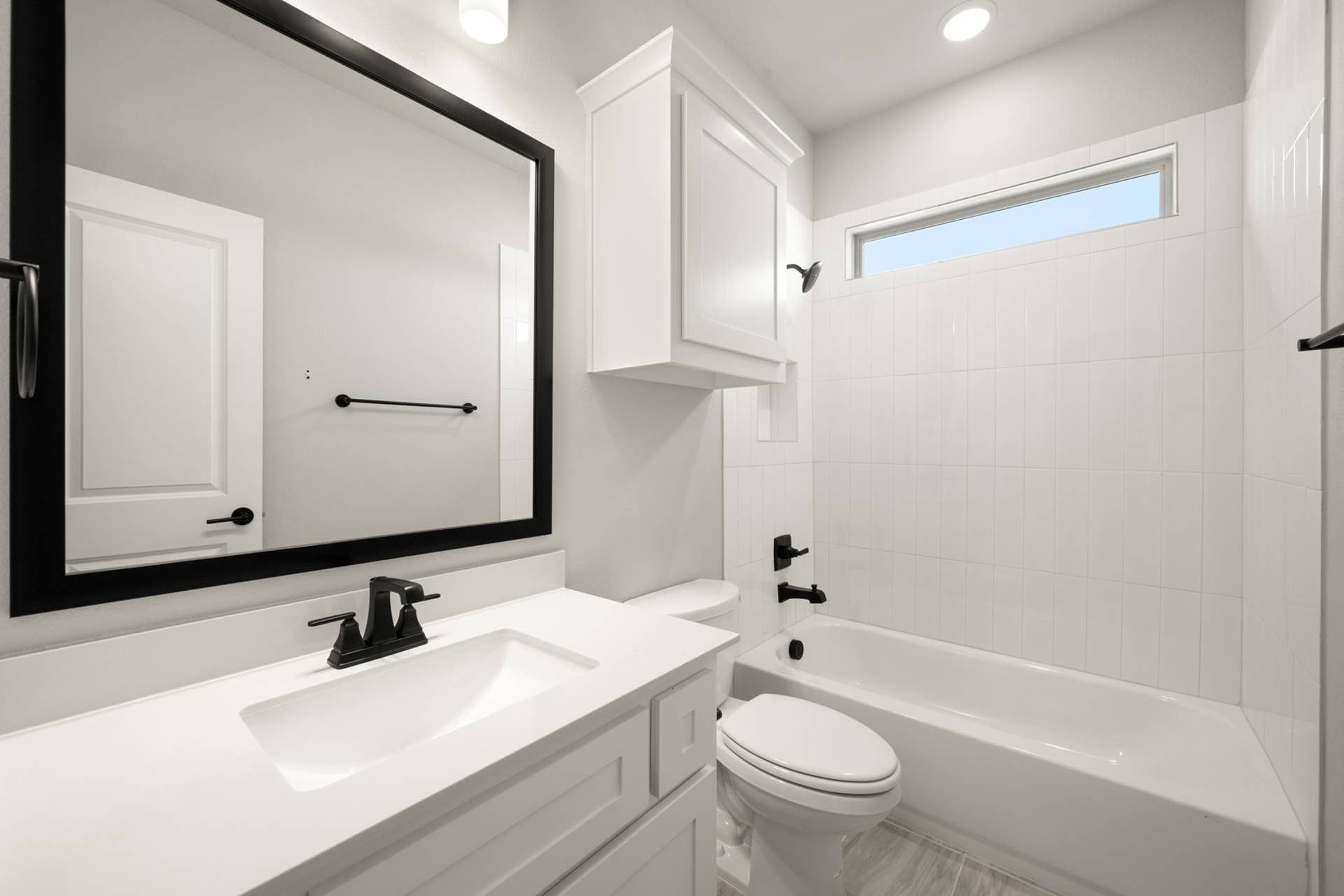 Modern bathroom with white cabinetry, black fixtures, and a large mirror.