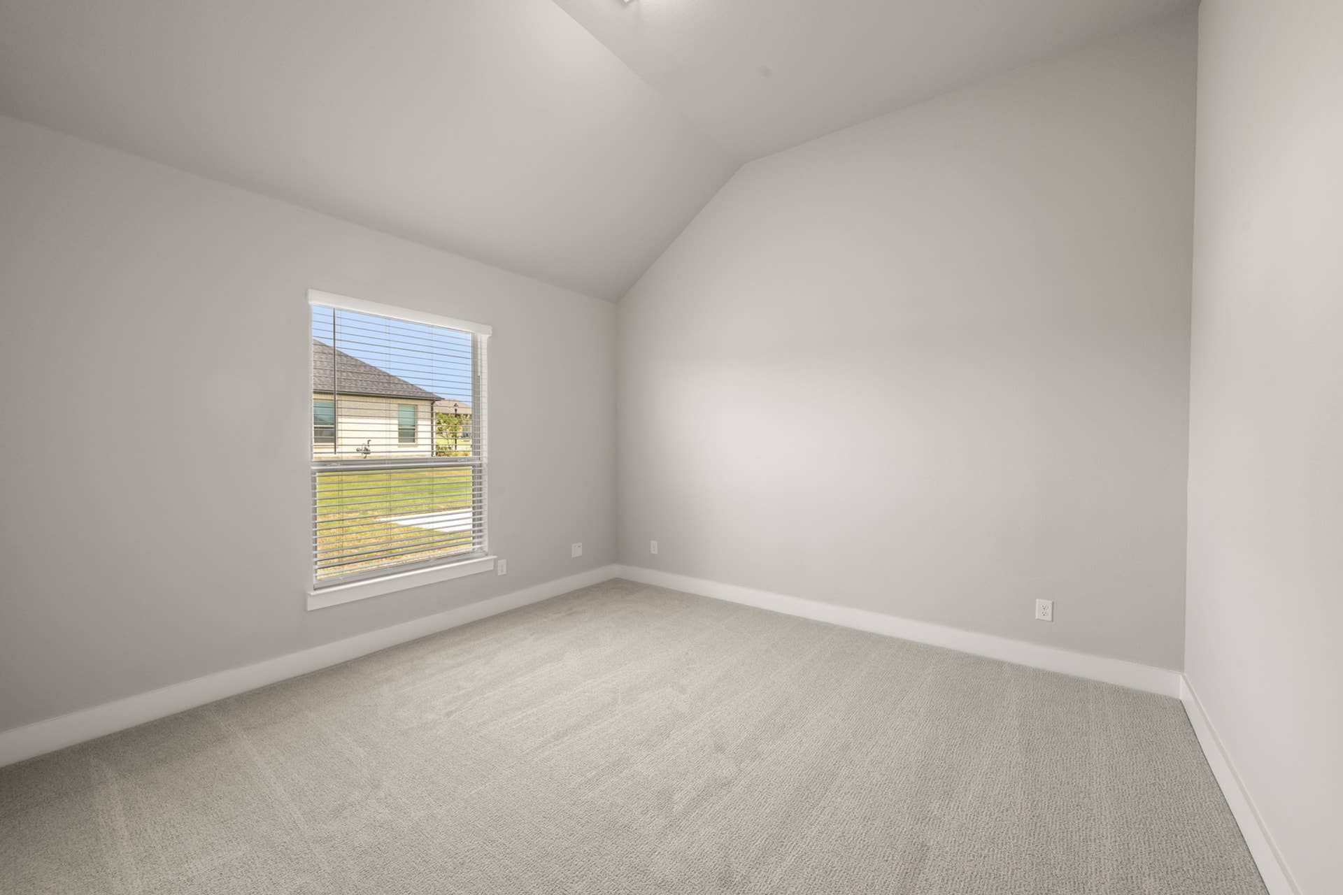 Spacious bedroom with vaulted ceiling and large window overlooking the outdoors.