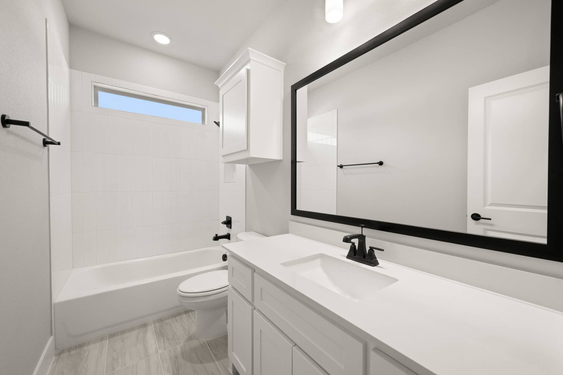 Modern bathroom with white cabinetry, black fixtures, and large mirror.