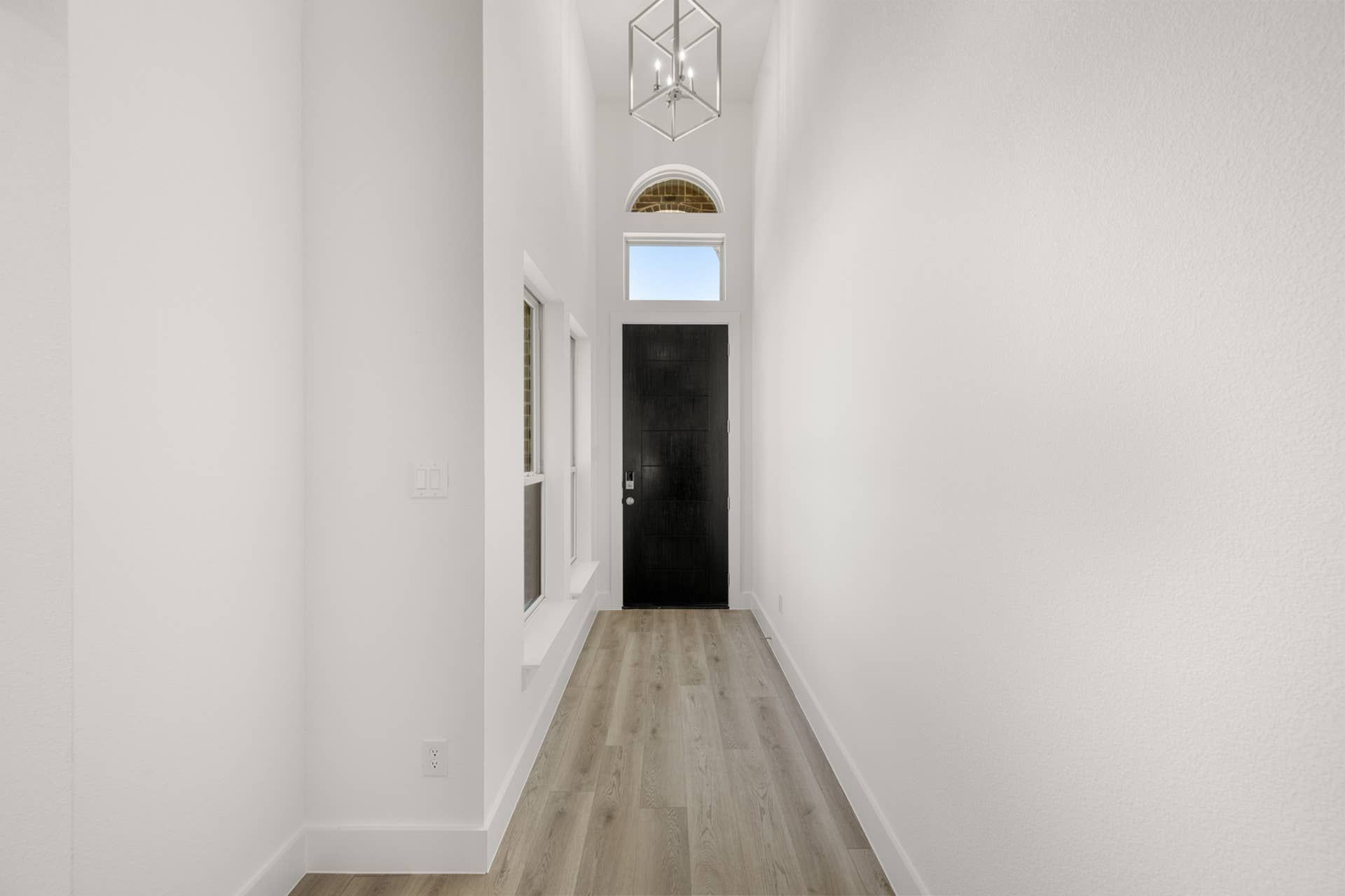 Bright entryway with wood flooring, modern light fixture, and dark front door.