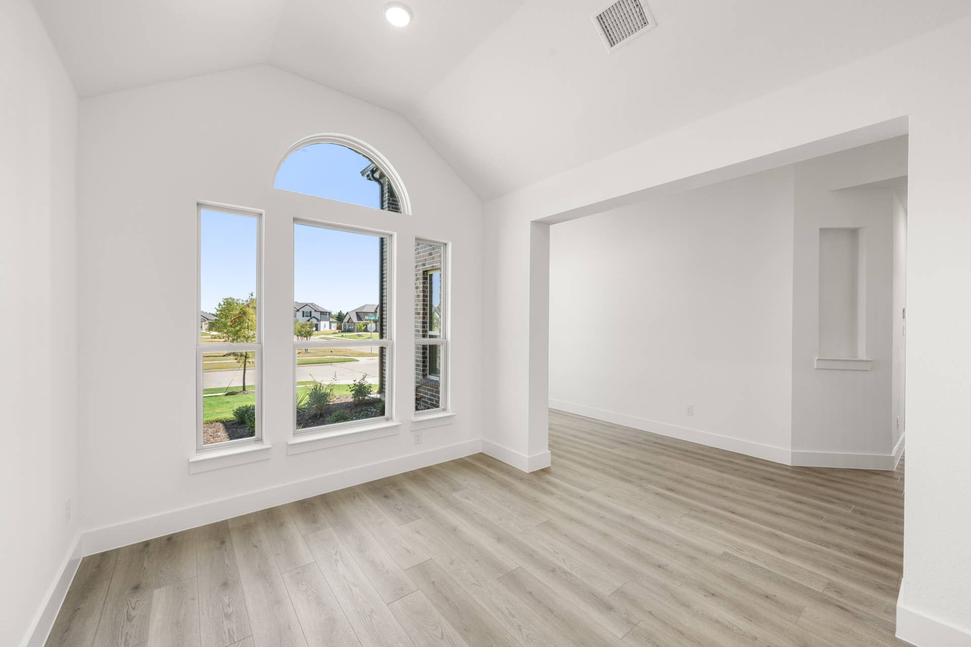 Bright dining room with large arched window and wood flooring.