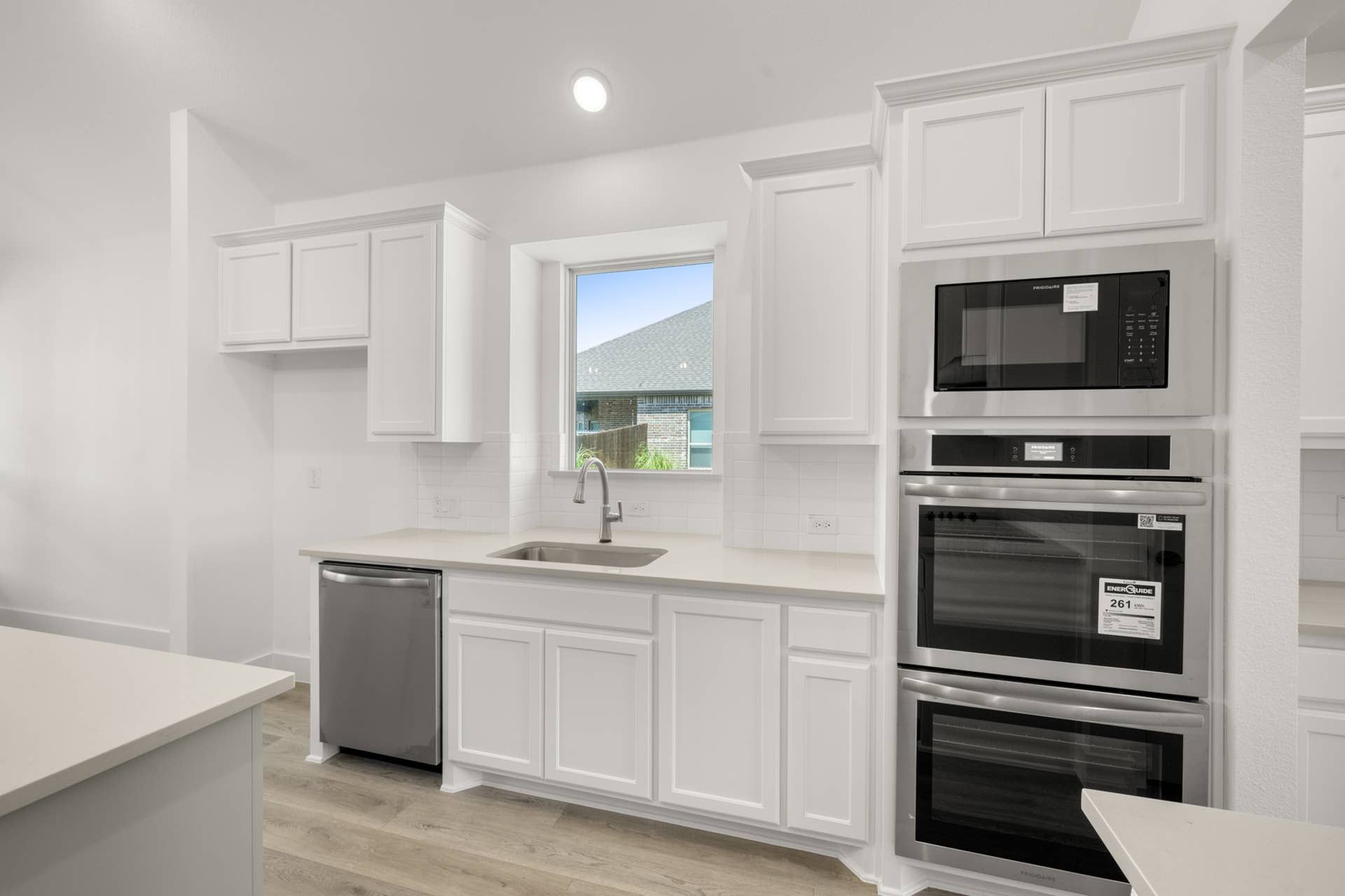 Modern kitchen with white cabinetry, stainless steel appliances, and large window.