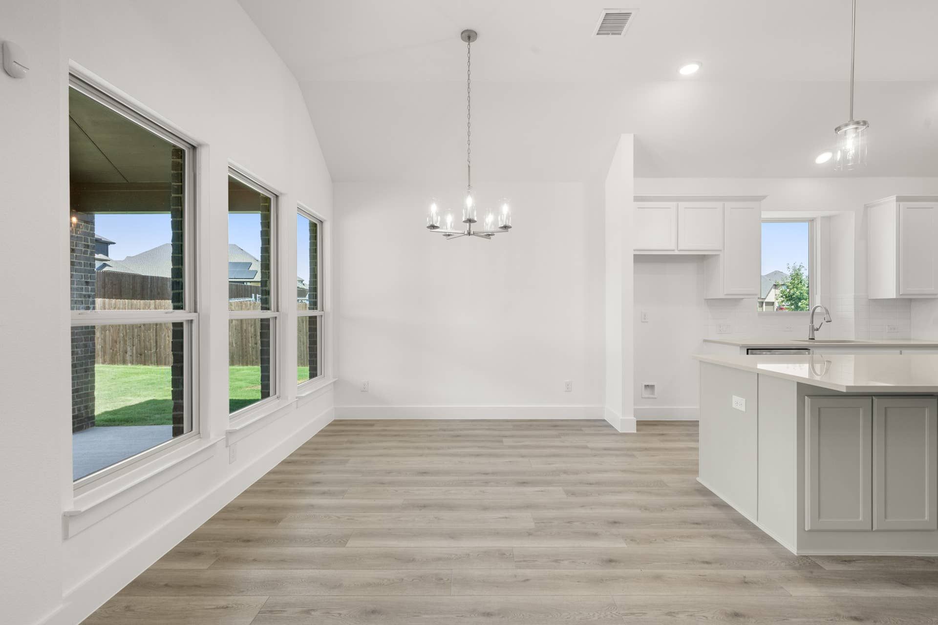 Spacious open-concept kitchen and dining area with modern chandelier and large windows.