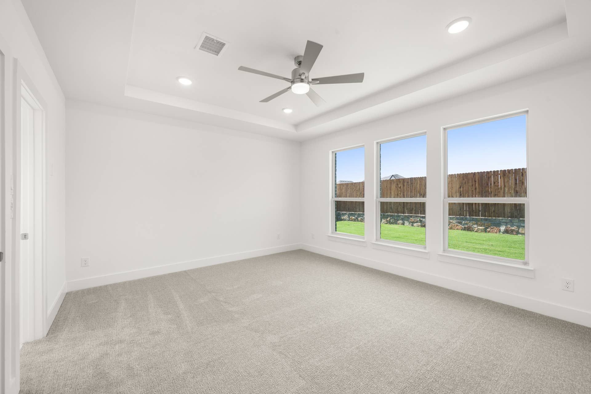 Spacious primary suite with large windows, ceiling fan, and neutral carpet flooring.