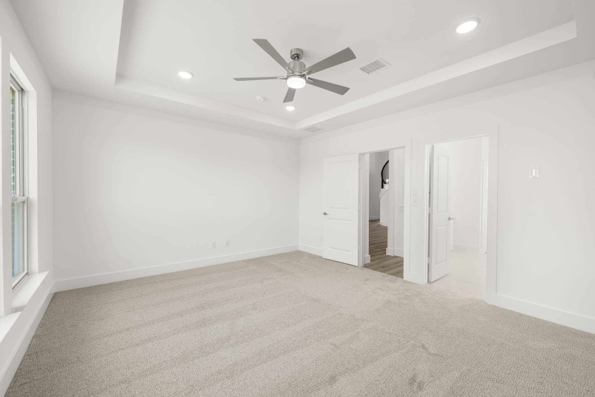 Spacious primary suite with tray ceiling, ceiling fan, and large window.