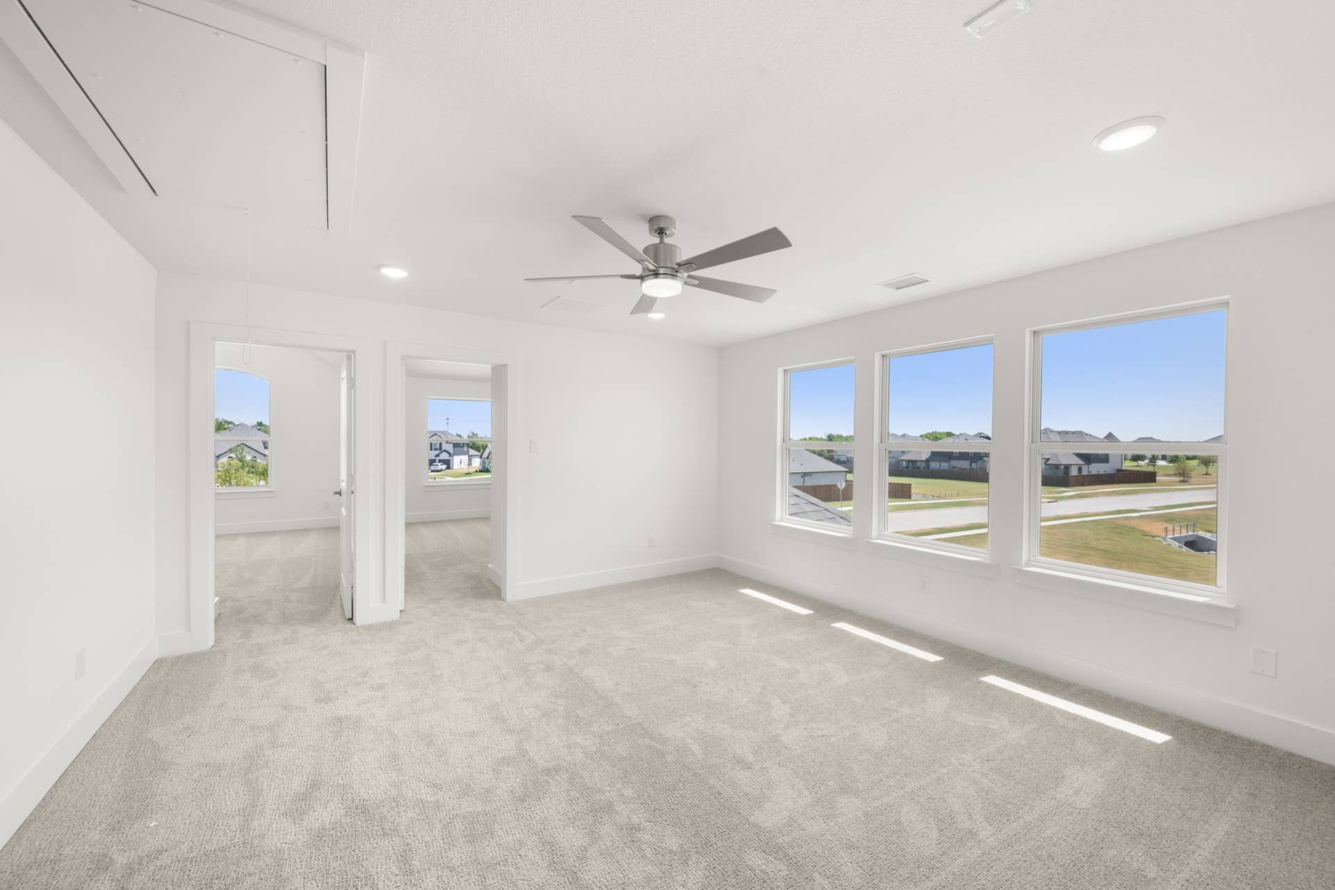 Spacious game room with carpet, ceiling fan, and large windows.