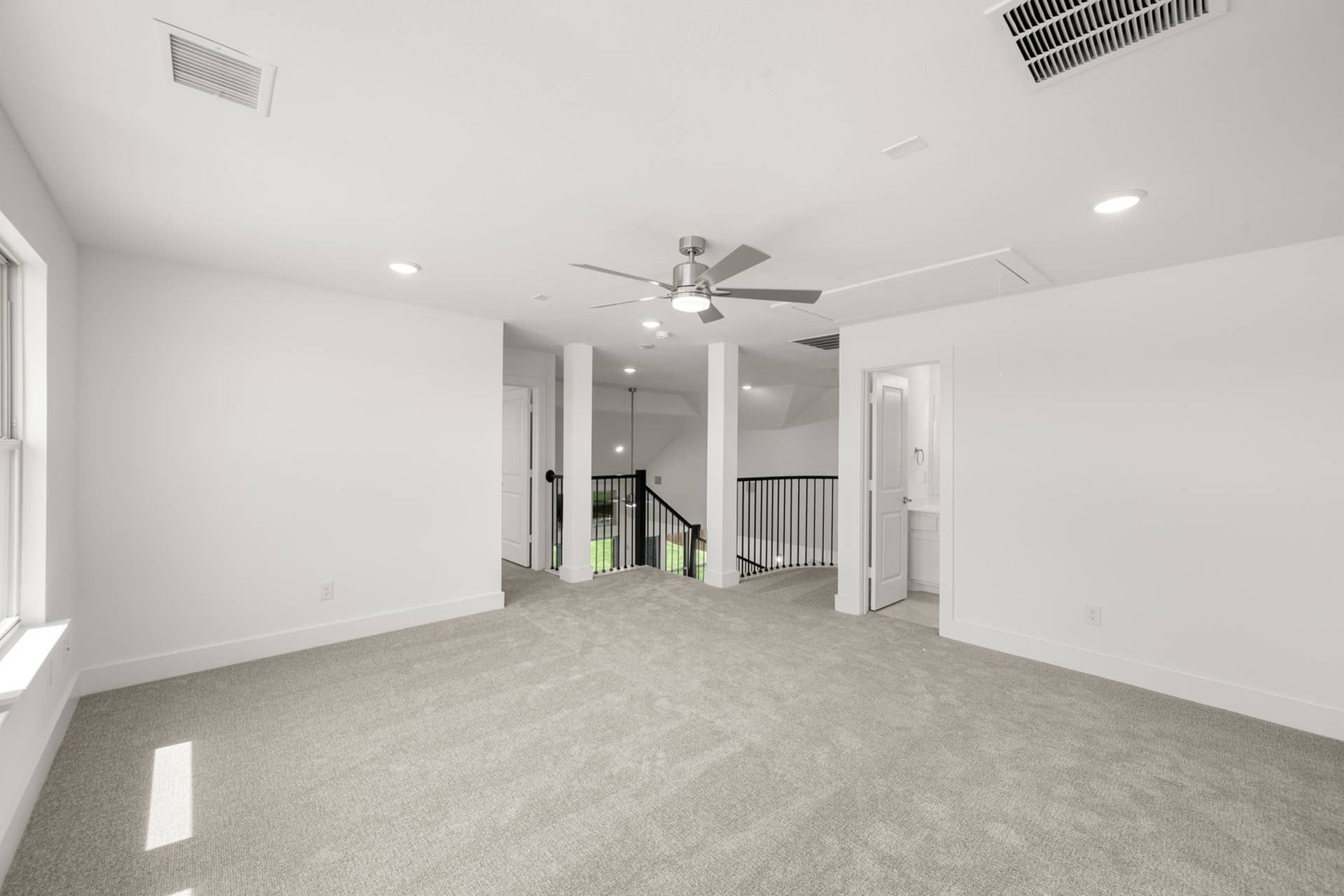 Spacious game room with ceiling fan, carpet flooring, and natural light.