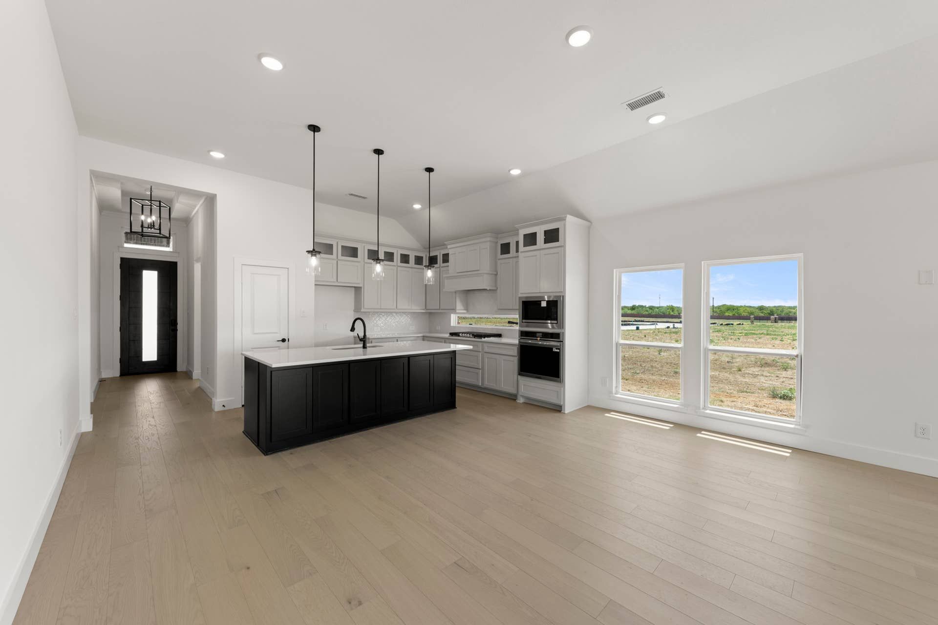 Modern kitchen with island, pendant lighting, and large windows overlooking outdoor landscape.