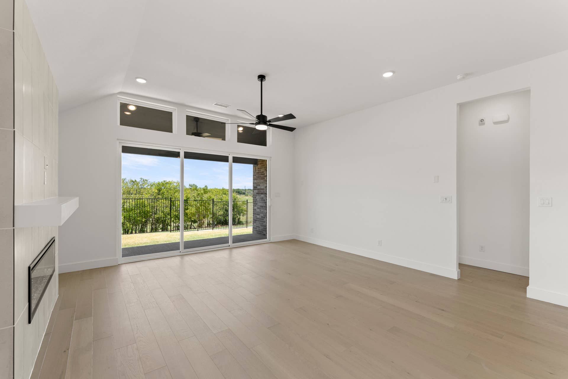 Spacious living room with large windows, hardwood floors, and modern ceiling fan.