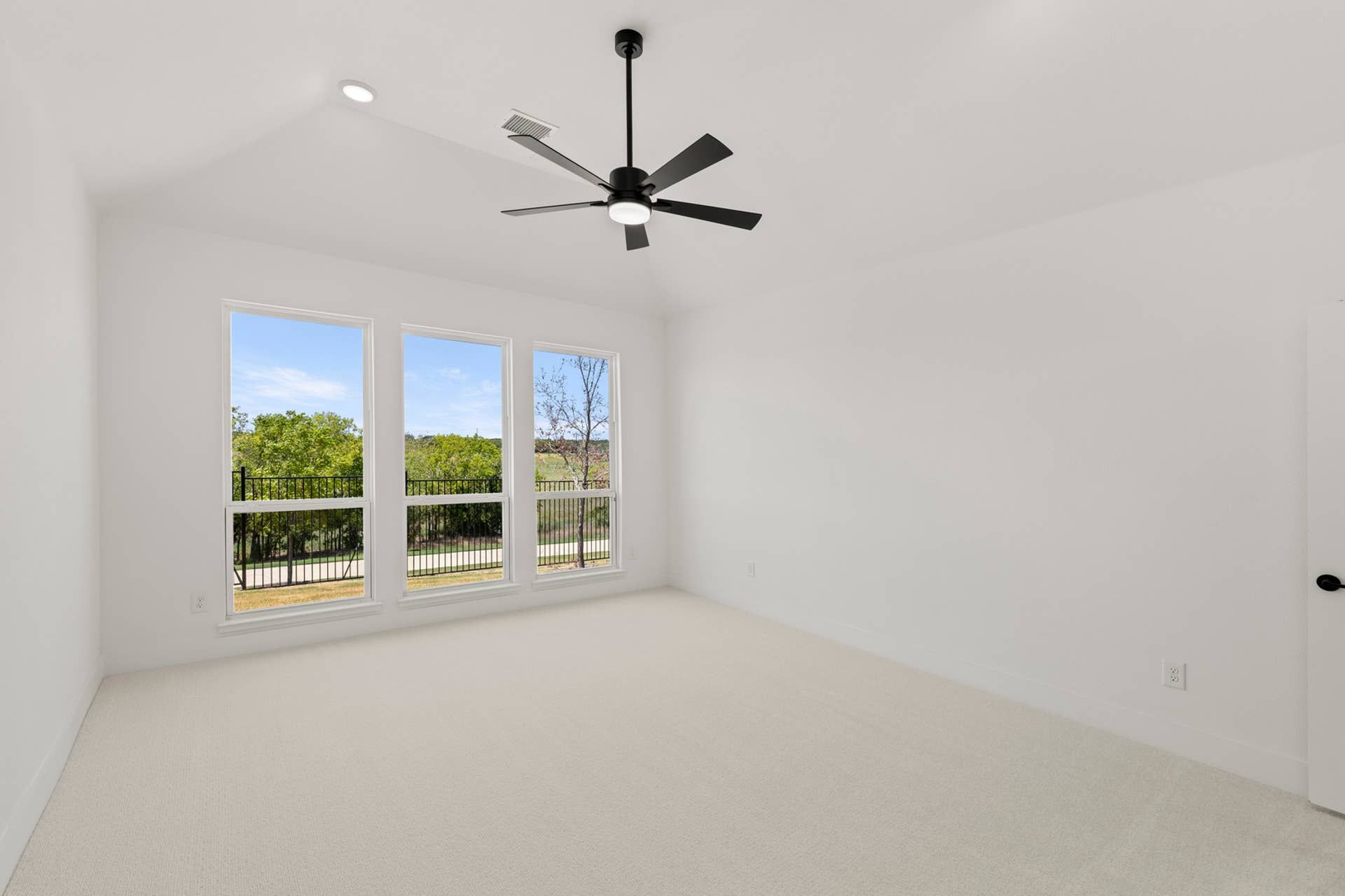 Spacious bedroom with large windows, ceiling fan, and neutral carpeting.