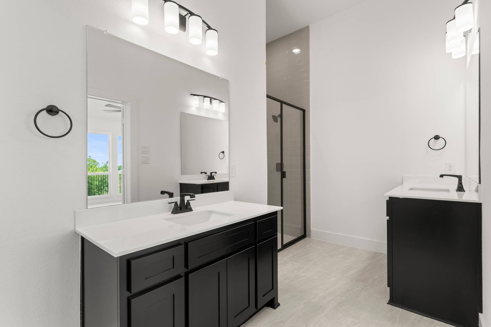 Modern bathroom with dual sinks, black cabinetry, and glass-enclosed shower.