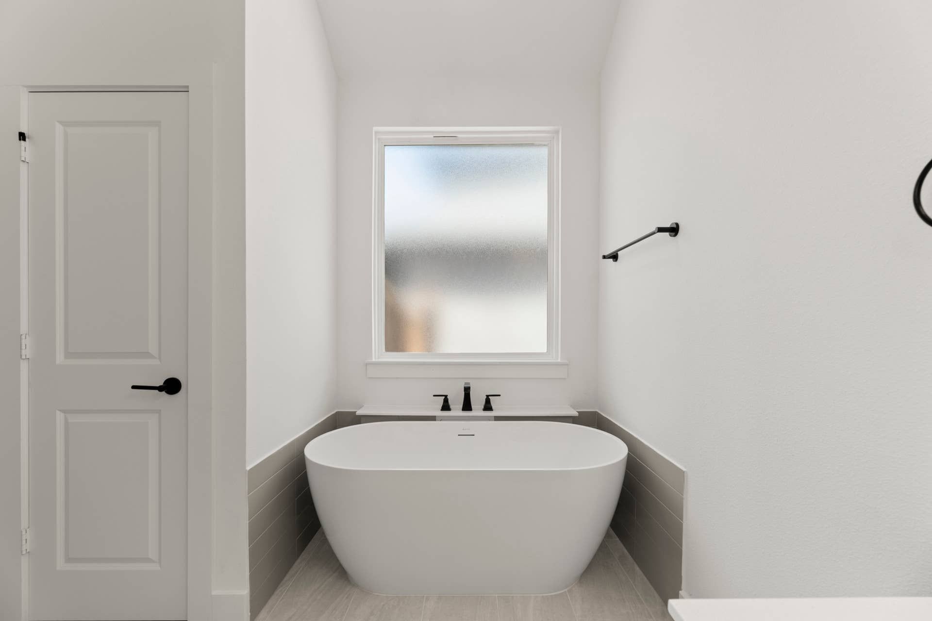Modern bathroom with freestanding tub and frosted window.