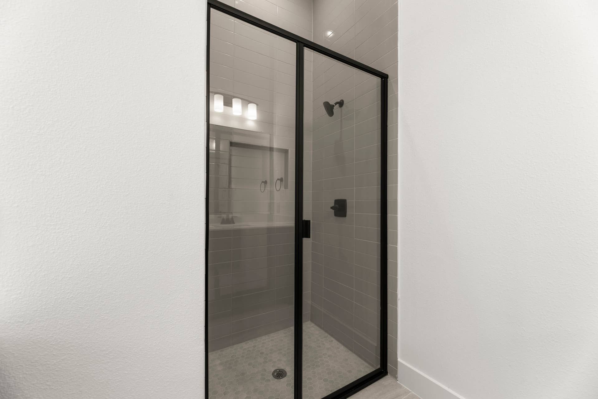 Modern bathroom shower with glass door and black frame accents.