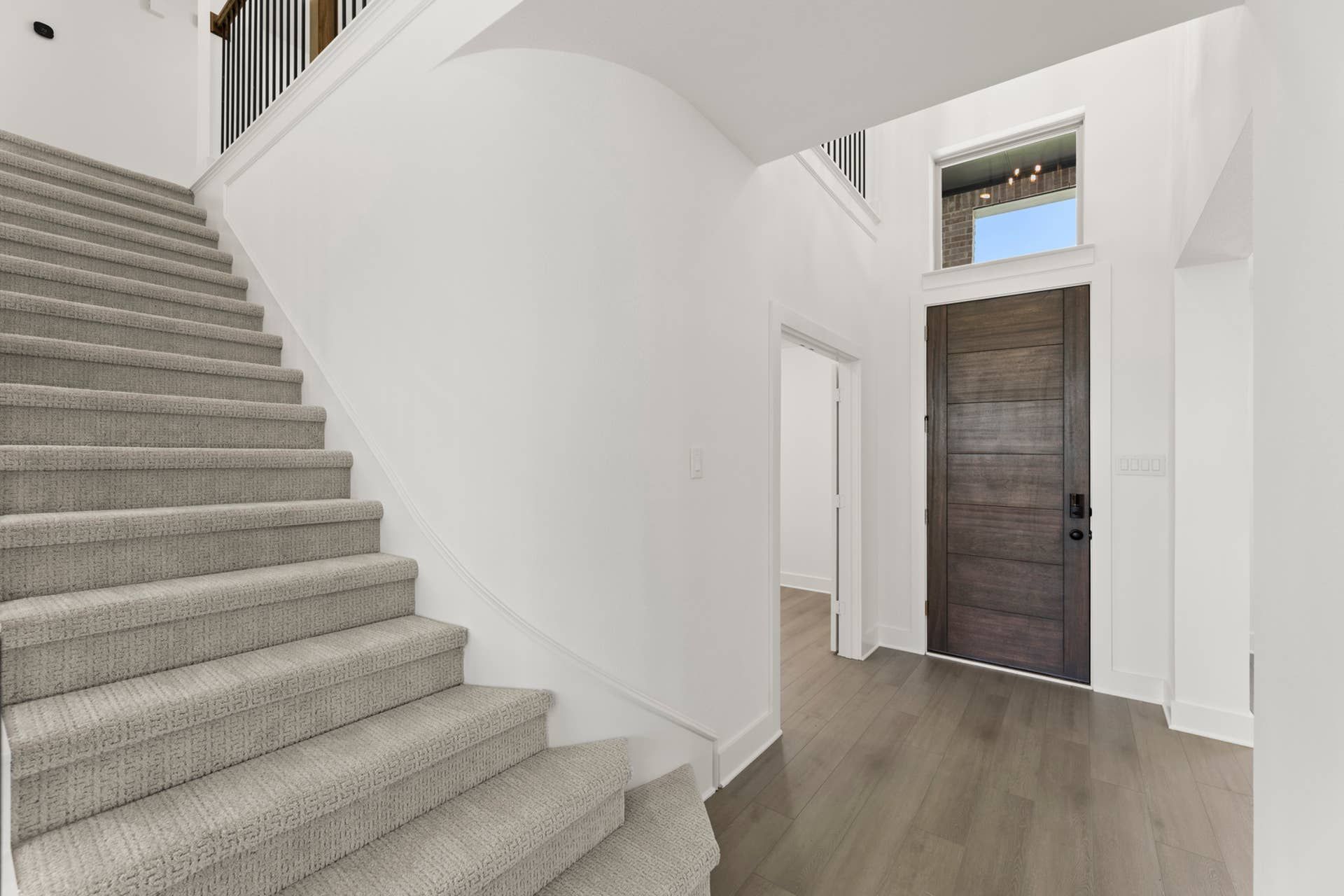 Modern entryway with wooden door and carpeted staircase.