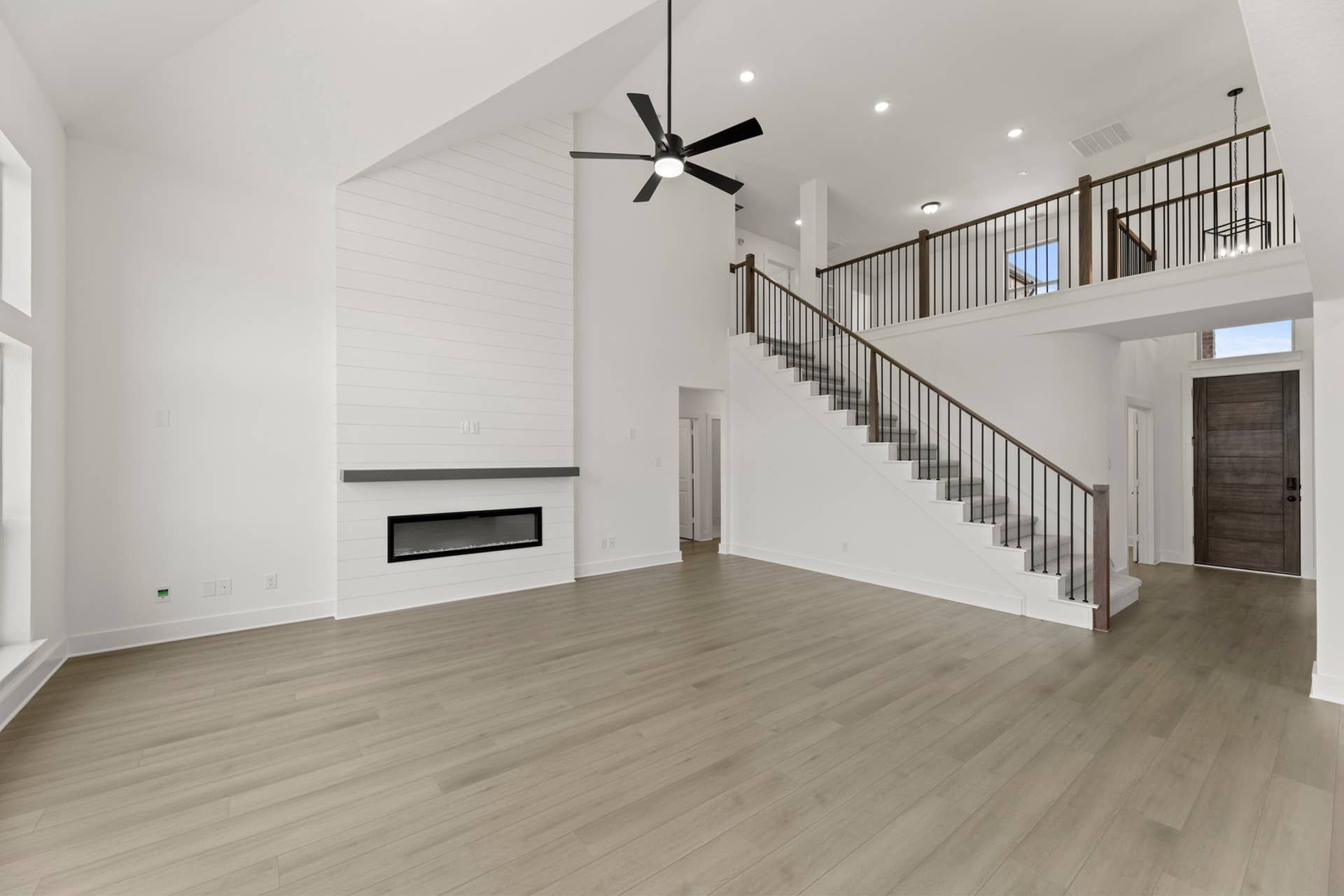 Spacious modern living room with high ceiling, staircase, and sleek fireplace.