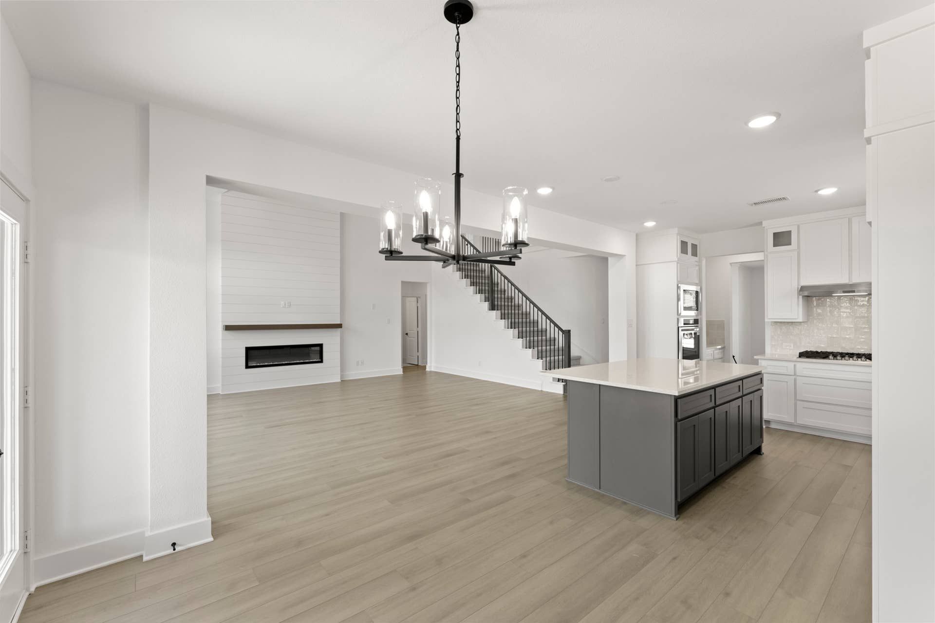 Spacious modern kitchen and living area with island, chandelier, and staircase.