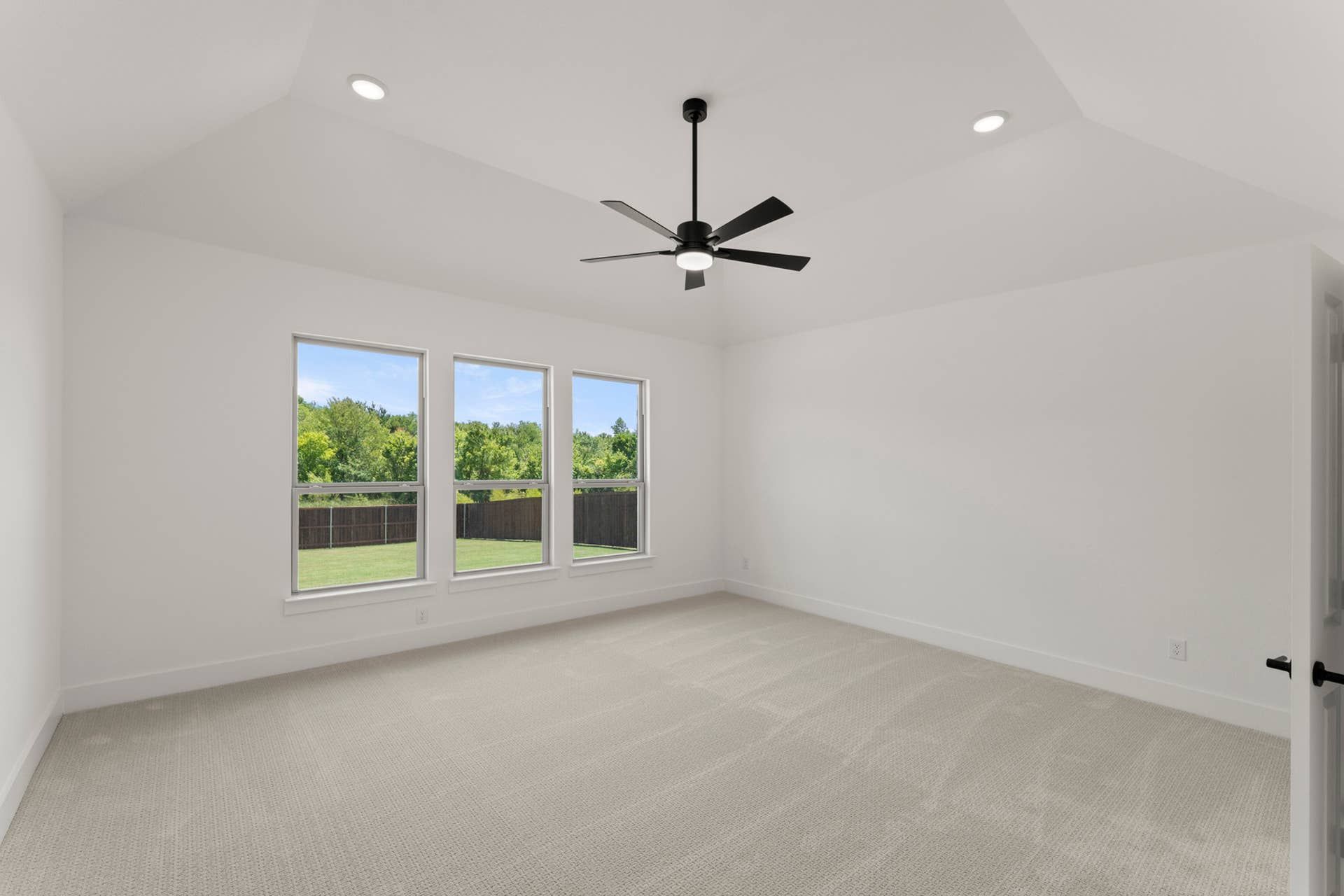 Spacious interior room with carpet, large windows, and modern ceiling fan.