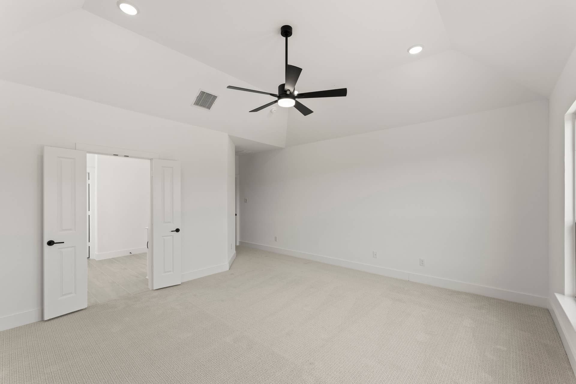 Spacious empty room with carpet flooring and modern ceiling fan.