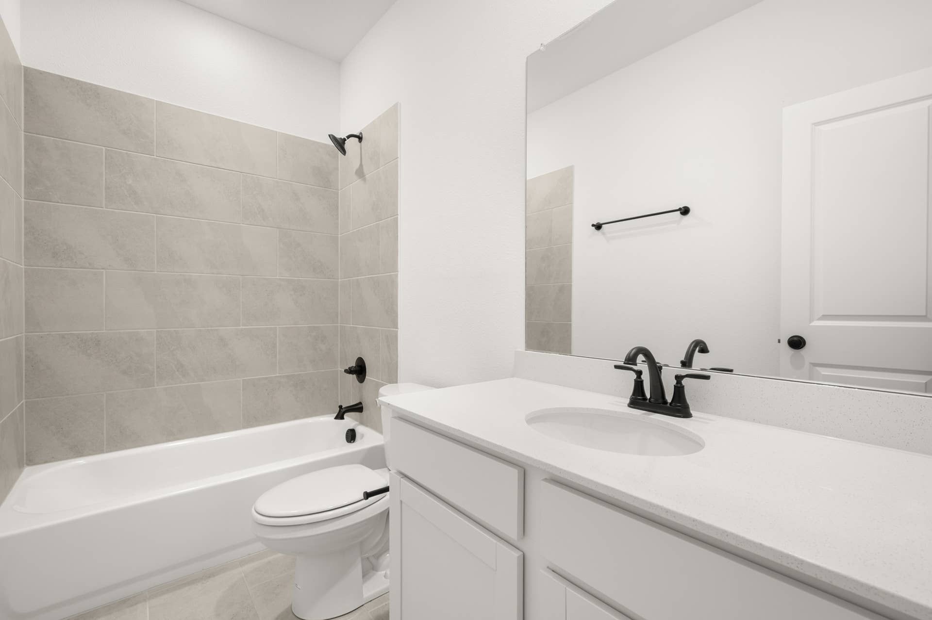 Modern bathroom with tiled shower, white vanity, and black fixtures.