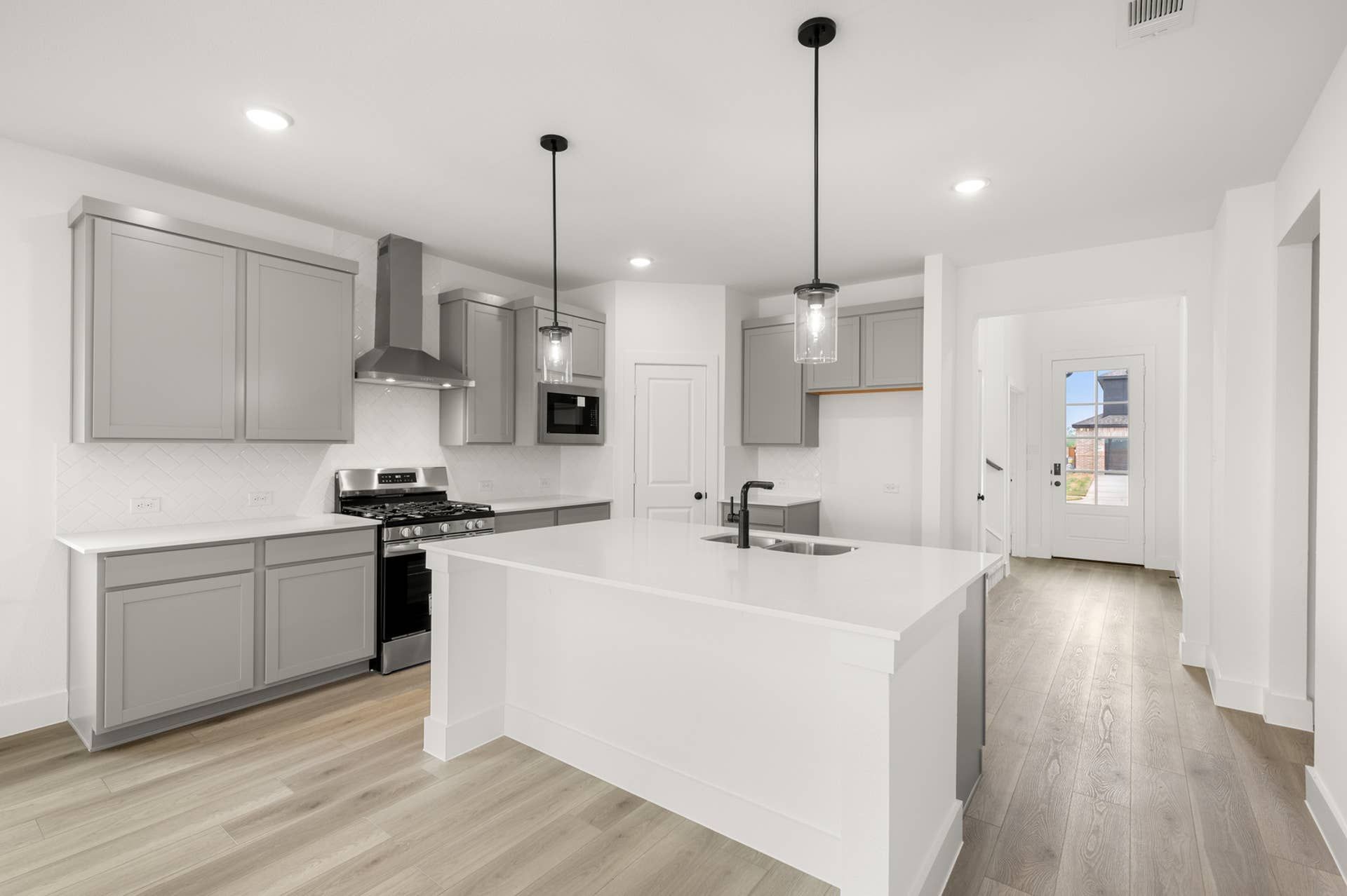 Modern kitchen with gray cabinets, large island, and pendant lighting.