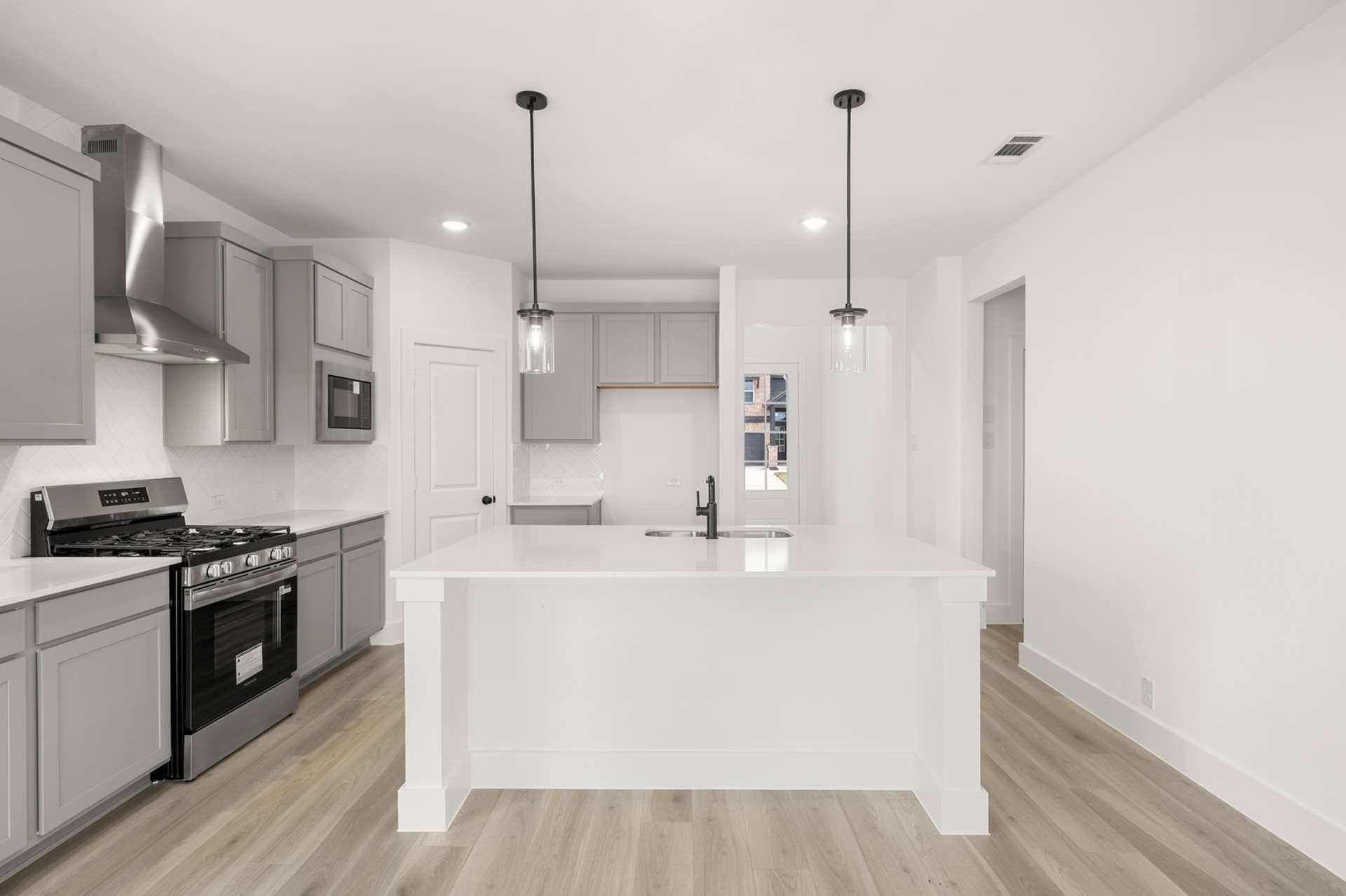 Modern kitchen with white island, pendant lights, and stainless steel appliances.