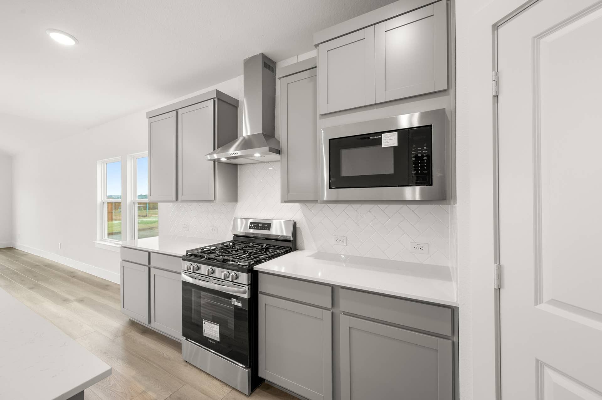 Modern kitchen with gray cabinets, stainless steel appliances, and herringbone tile backsplash.