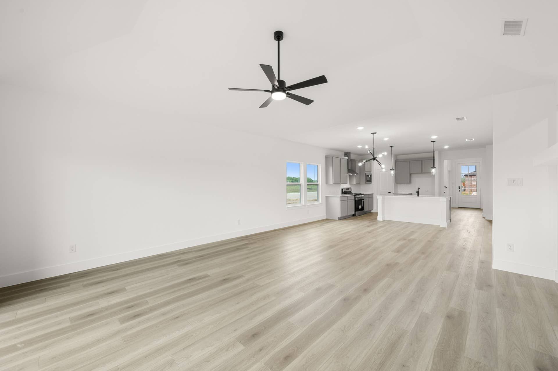Spacious living room with open kitchen, modern lighting, and large windows.