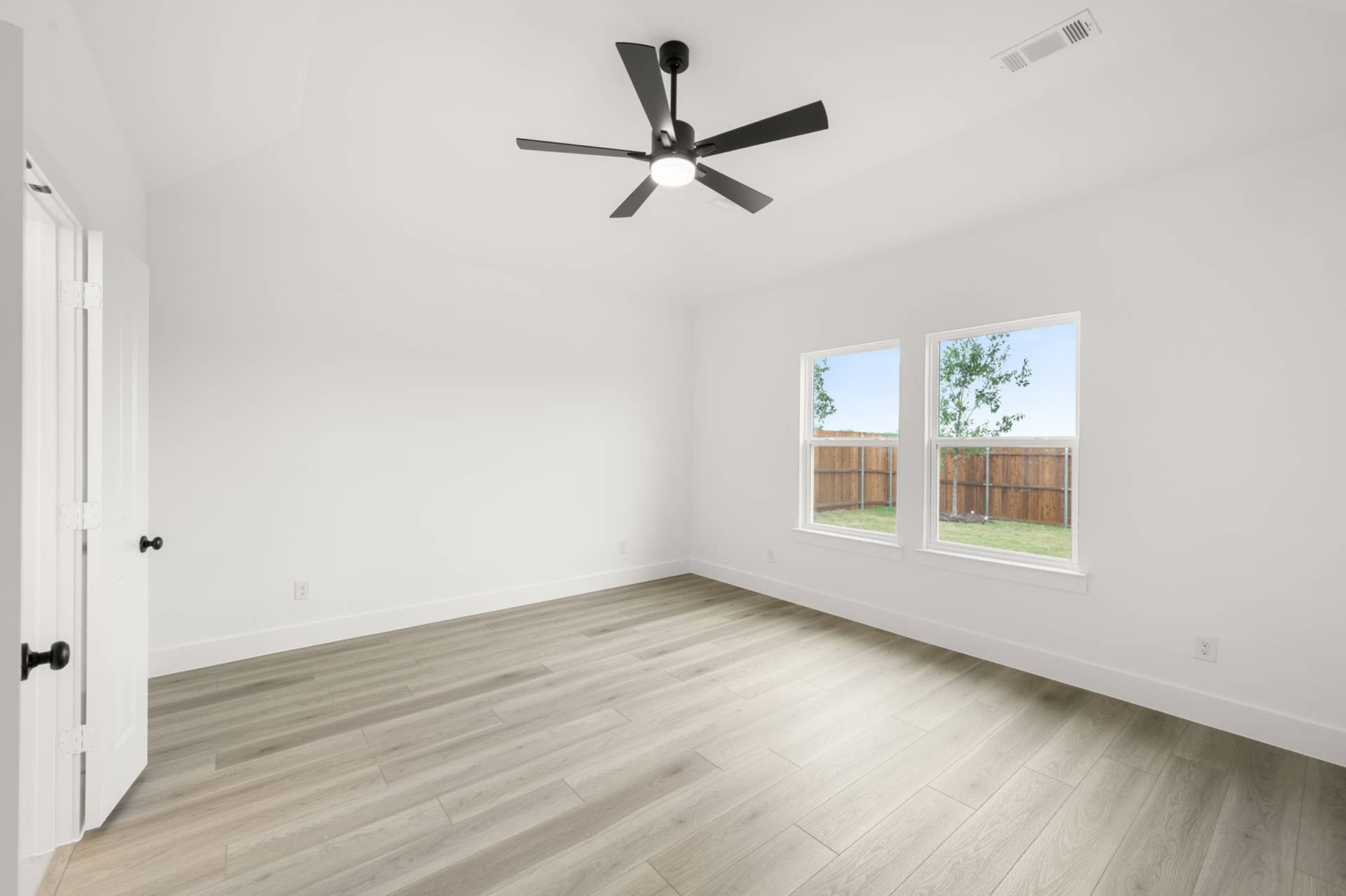 Spacious primary suite with ceiling fan and large windows overlooking fenced backyard.