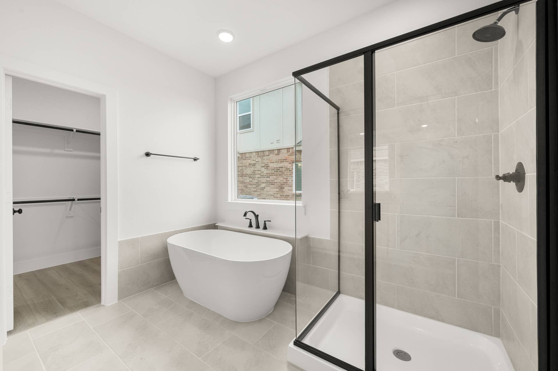 Modern bathroom with freestanding tub, glass shower, and walk-in closet entrance.