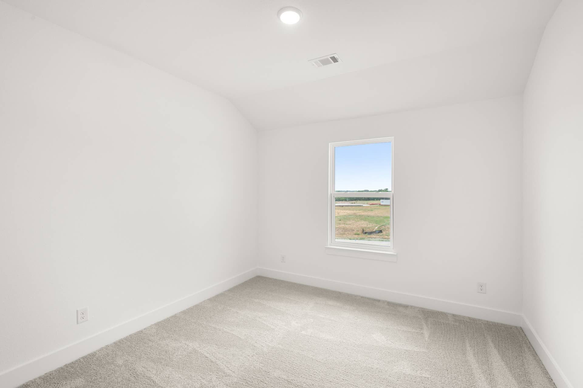 Bright, empty bedroom with carpet and single window overlooking landscape.