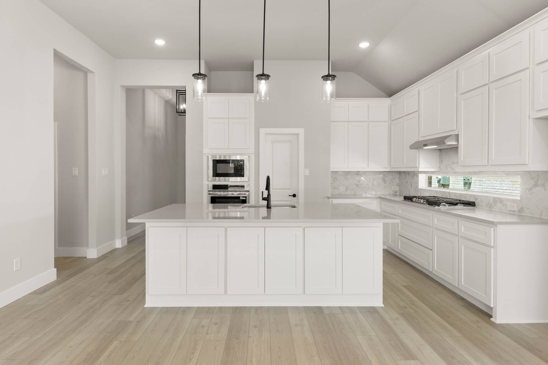 Modern kitchen with white cabinetry, marble backsplash, and pendant lighting.