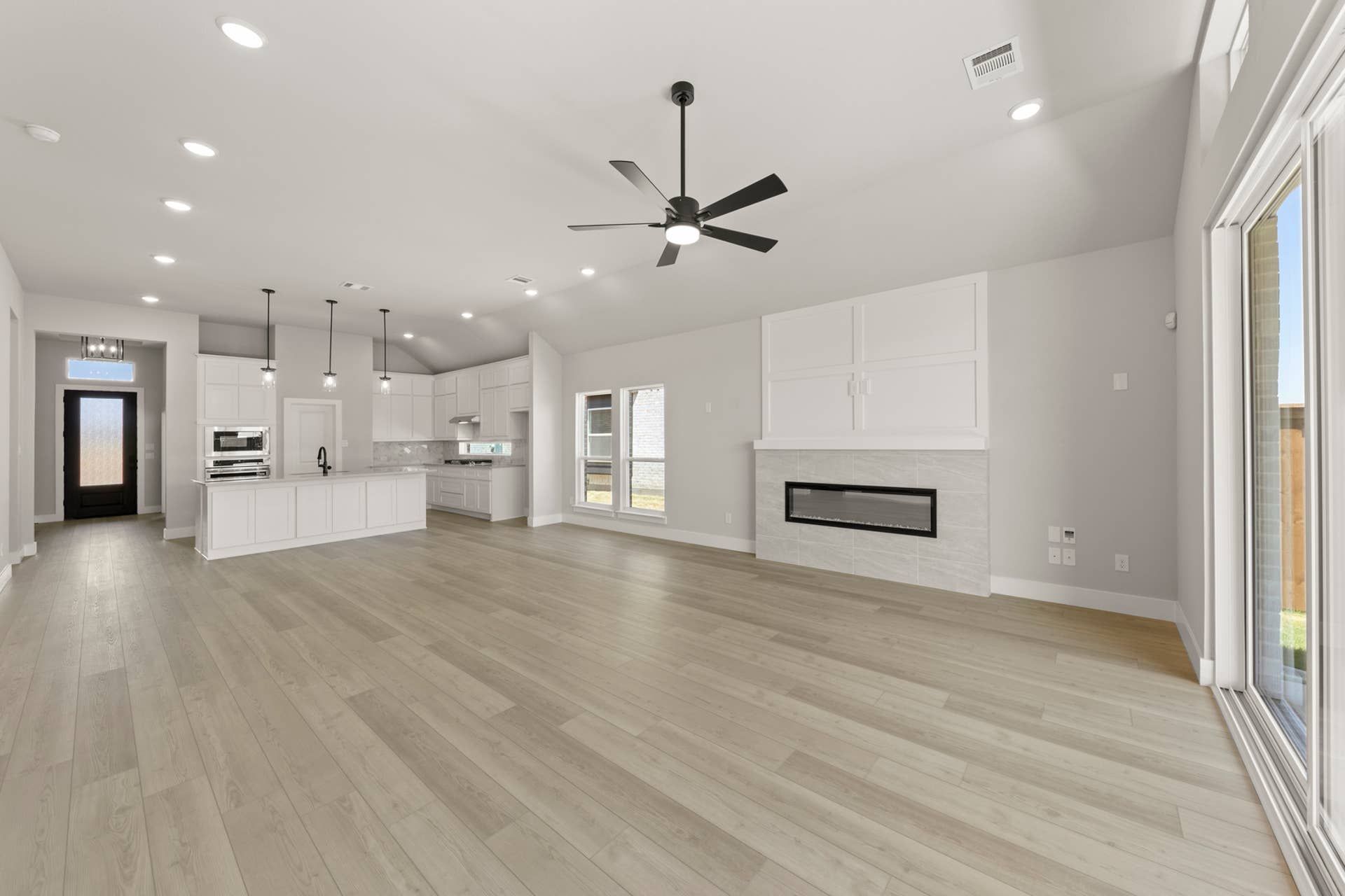 Spacious modern open-plan kitchen and living area with sleek fireplace and ceiling fan.