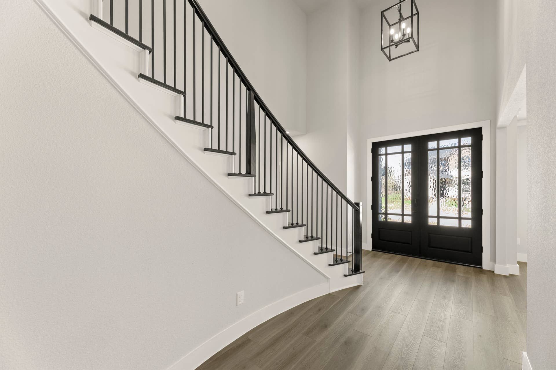 Elegant entryway with curved staircase and modern glass-paneled double doors.