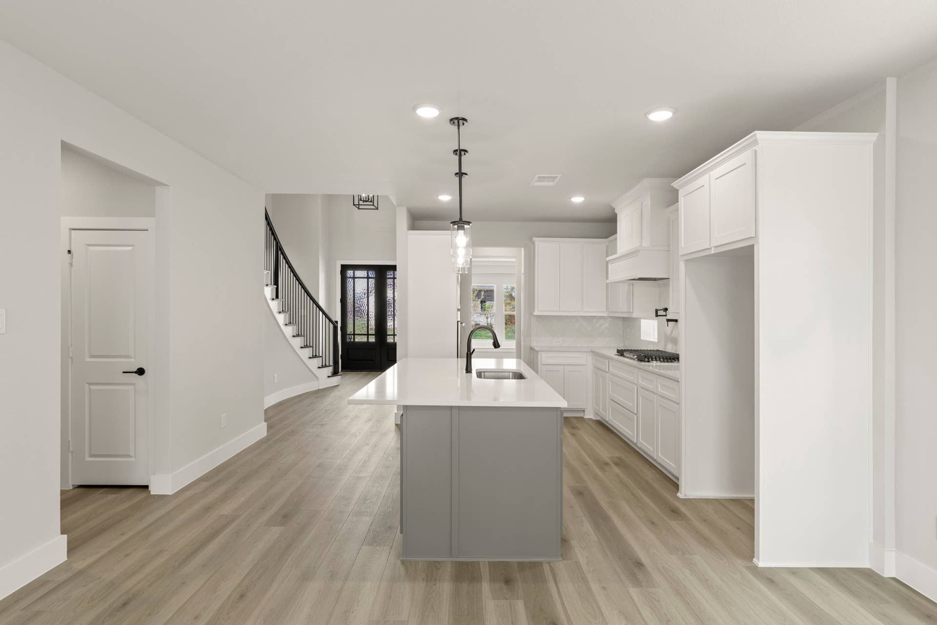 Modern kitchen with white cabinetry, island, and elegant staircase in open-concept layout.