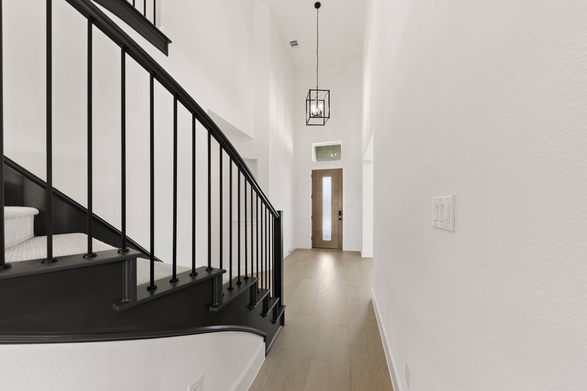 Modern entryway with curved staircase and pendant lighting.