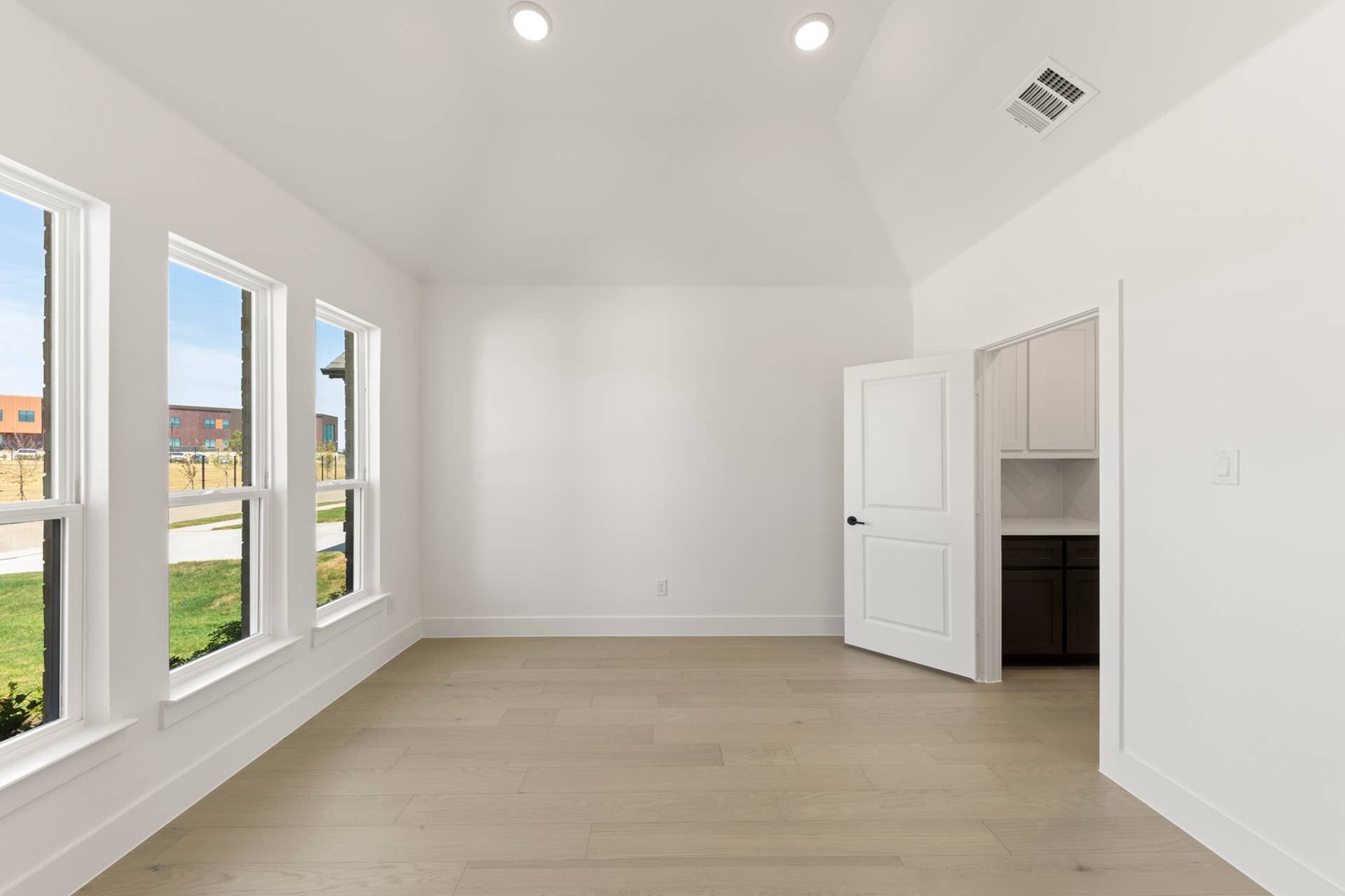 Bright dining room with large windows, wooden floors, and open door to kitchen.