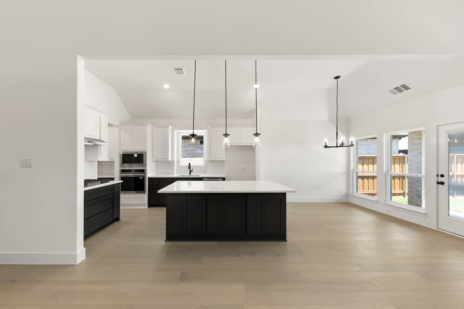Modern kitchen with black island, pendant lights, and large windows.
