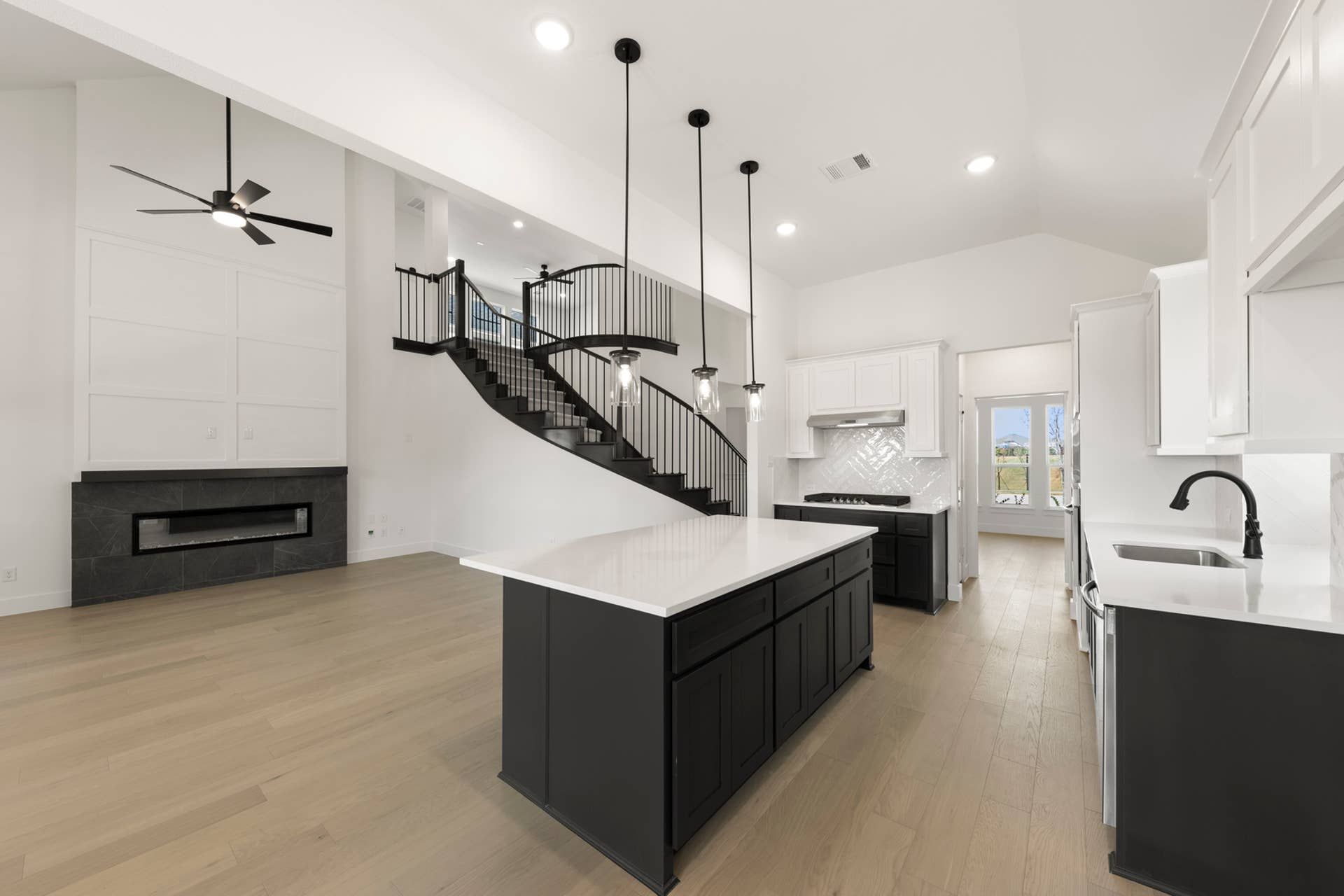 Modern kitchen interior with island, pendant lights, and curved staircase.