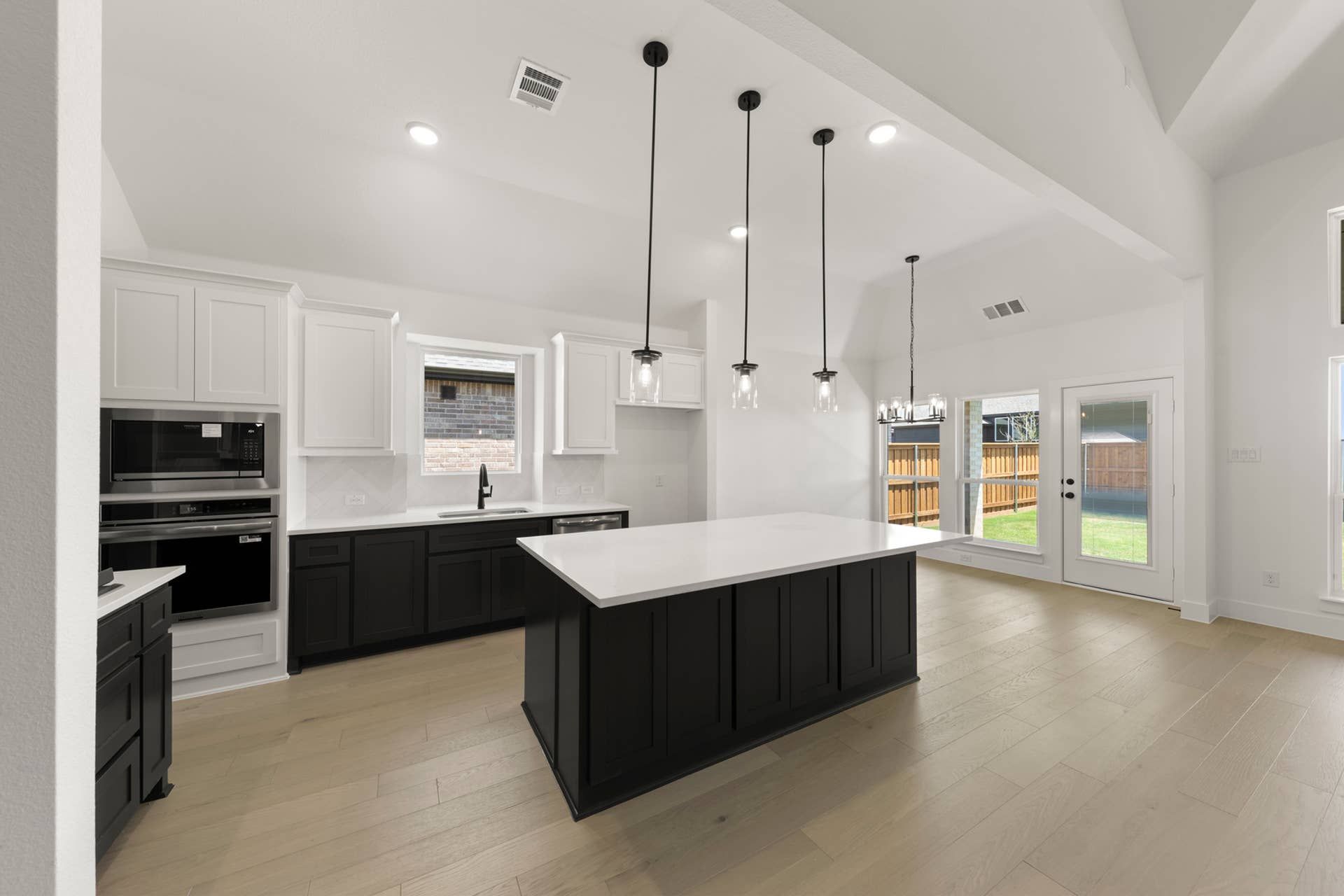 Modern kitchen with white cabinets, black island, pendant lights, and wood flooring.
