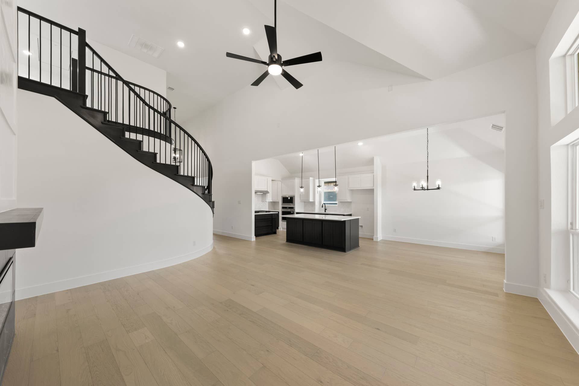 Spacious modern interior with curved staircase, open kitchen, and light wood floors.