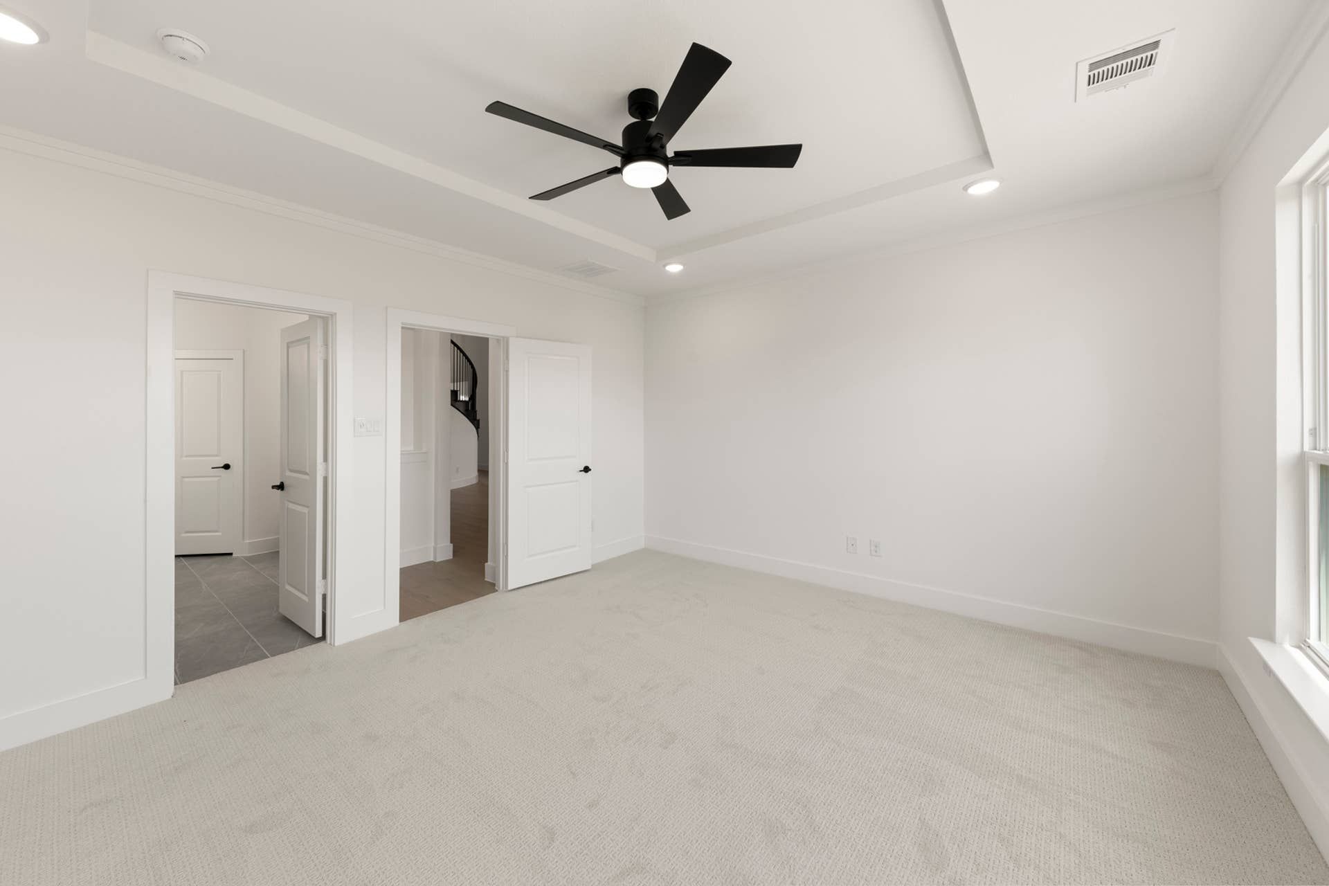 Spacious bedroom with ceiling fan, carpet, and bright natural light.