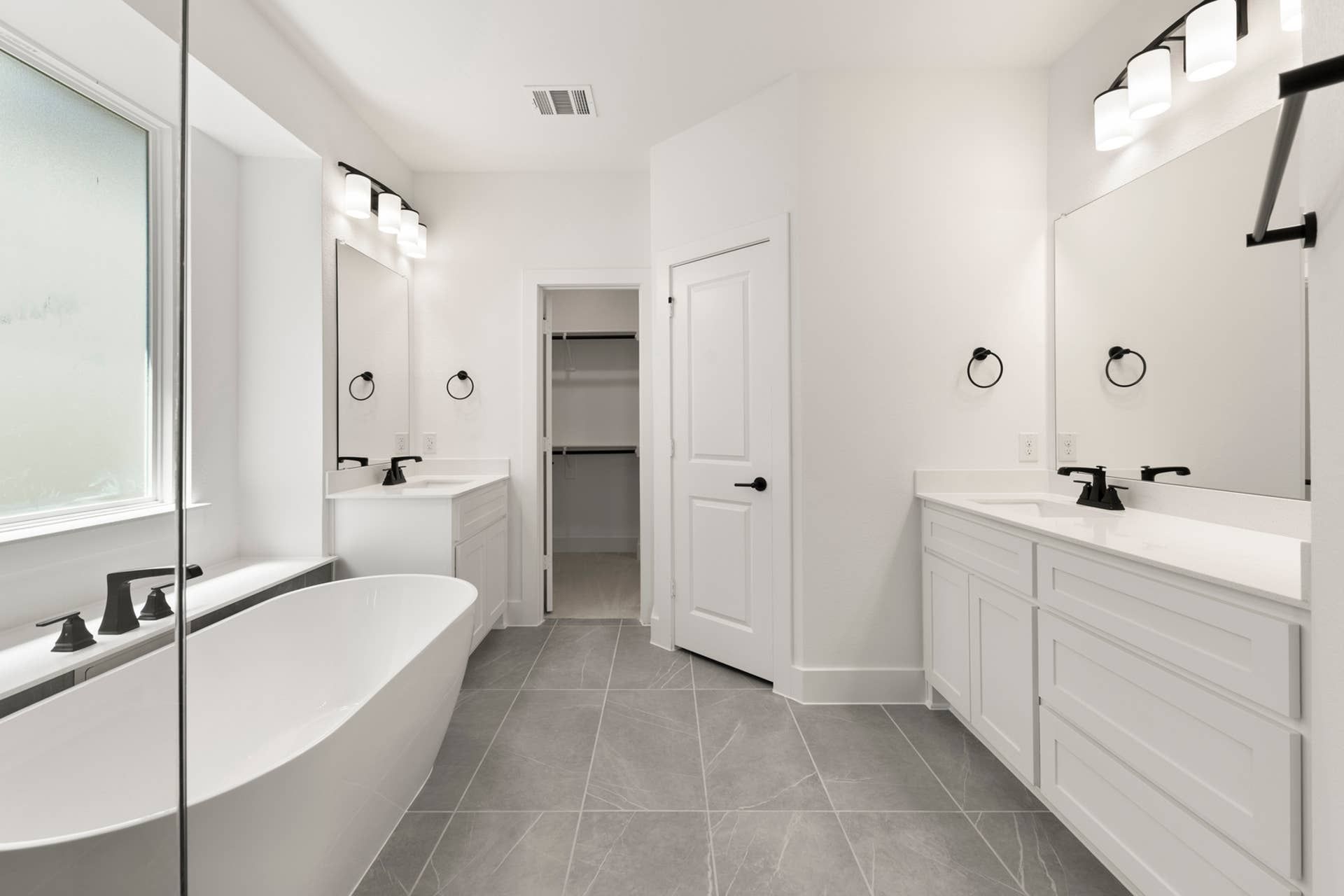 Modern bathroom with freestanding tub, dual vanities, and large mirrors.