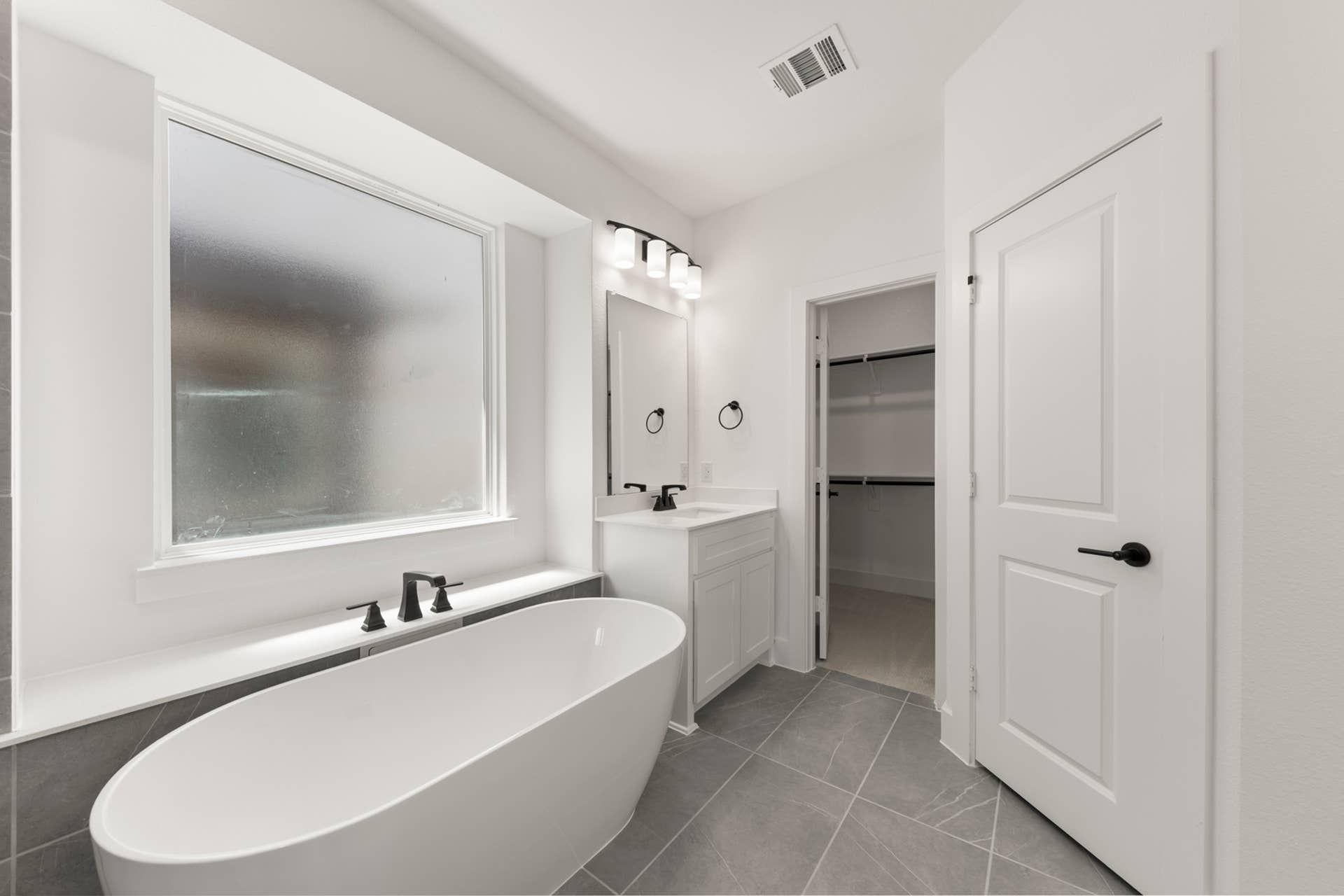 Modern bathroom with freestanding tub, large window, and walk-in closet.