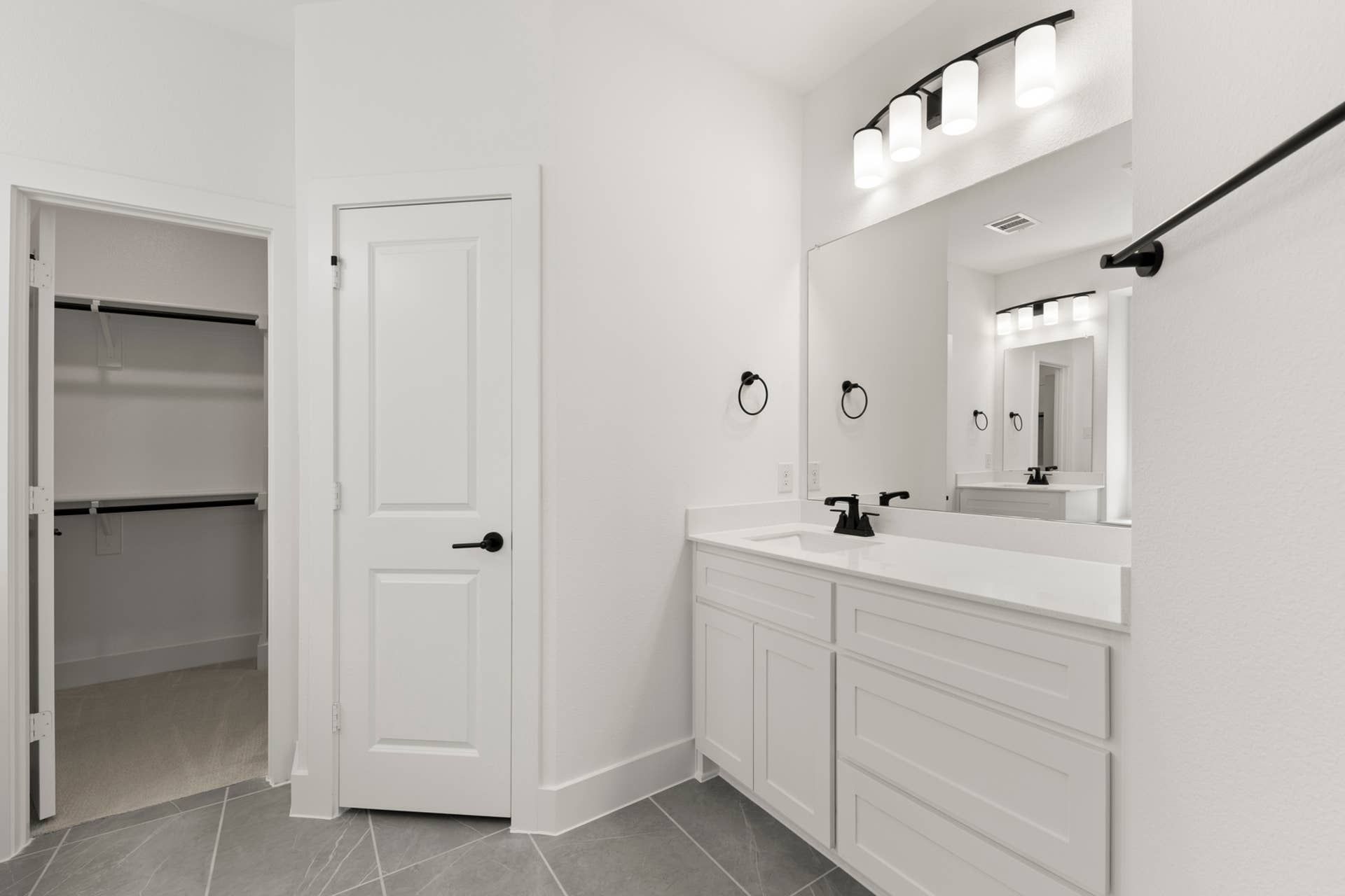 Modern bathroom with sleek vanity, large mirror, and walk-in closet access.
