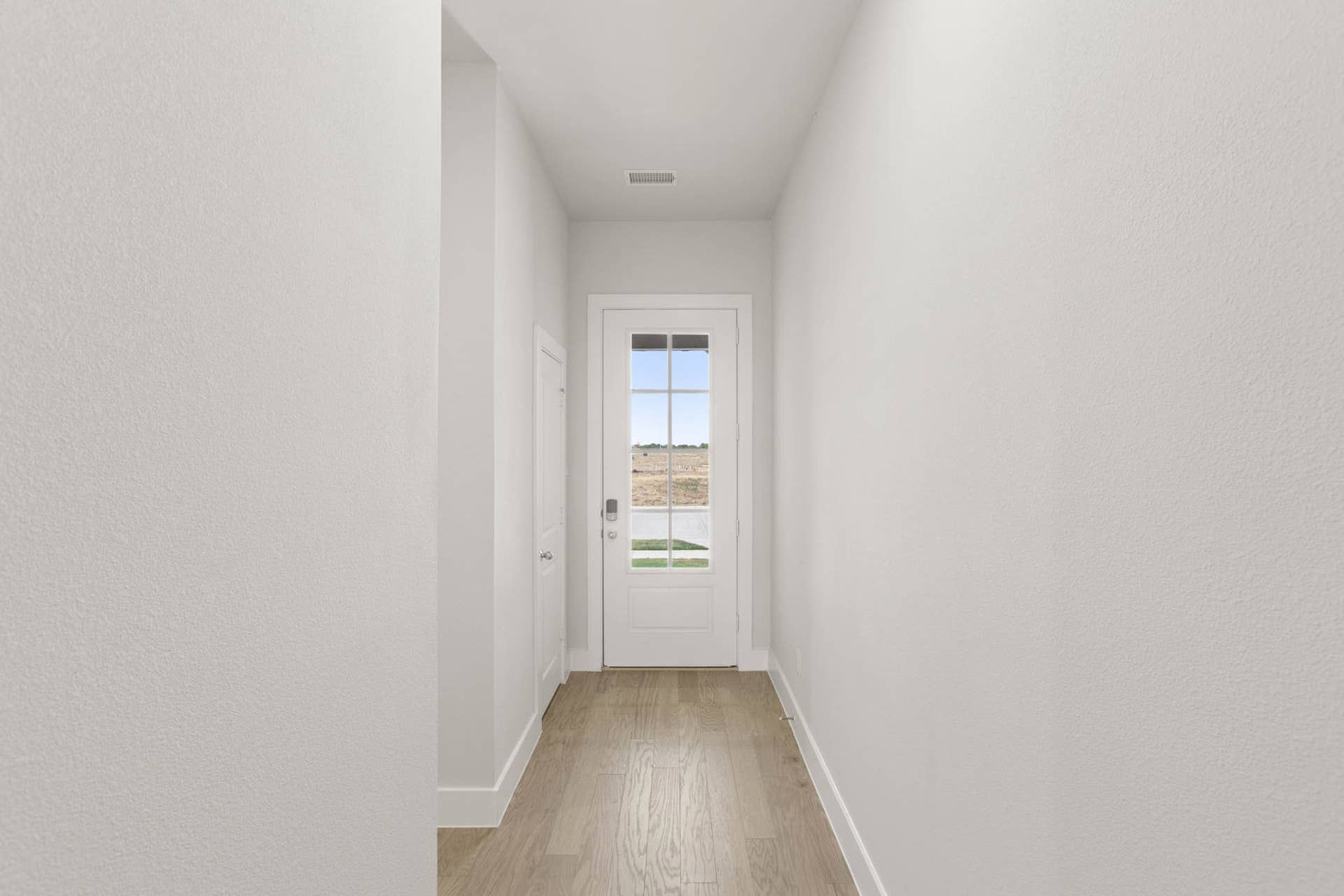 Bright hallway with wooden floor leading to glass-panel door view.