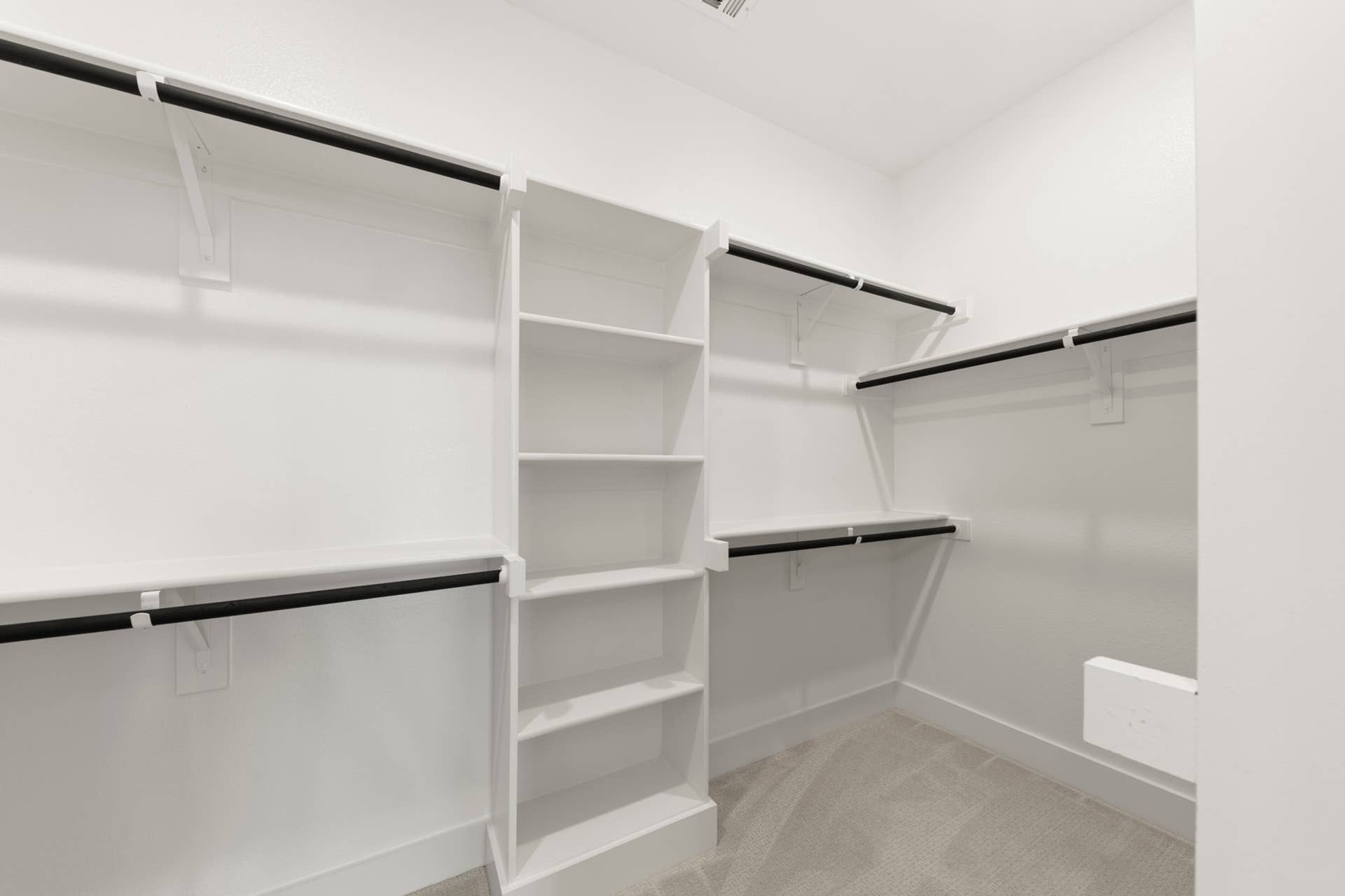 Spacious walk-in closet with white shelves and multiple hanging rods.