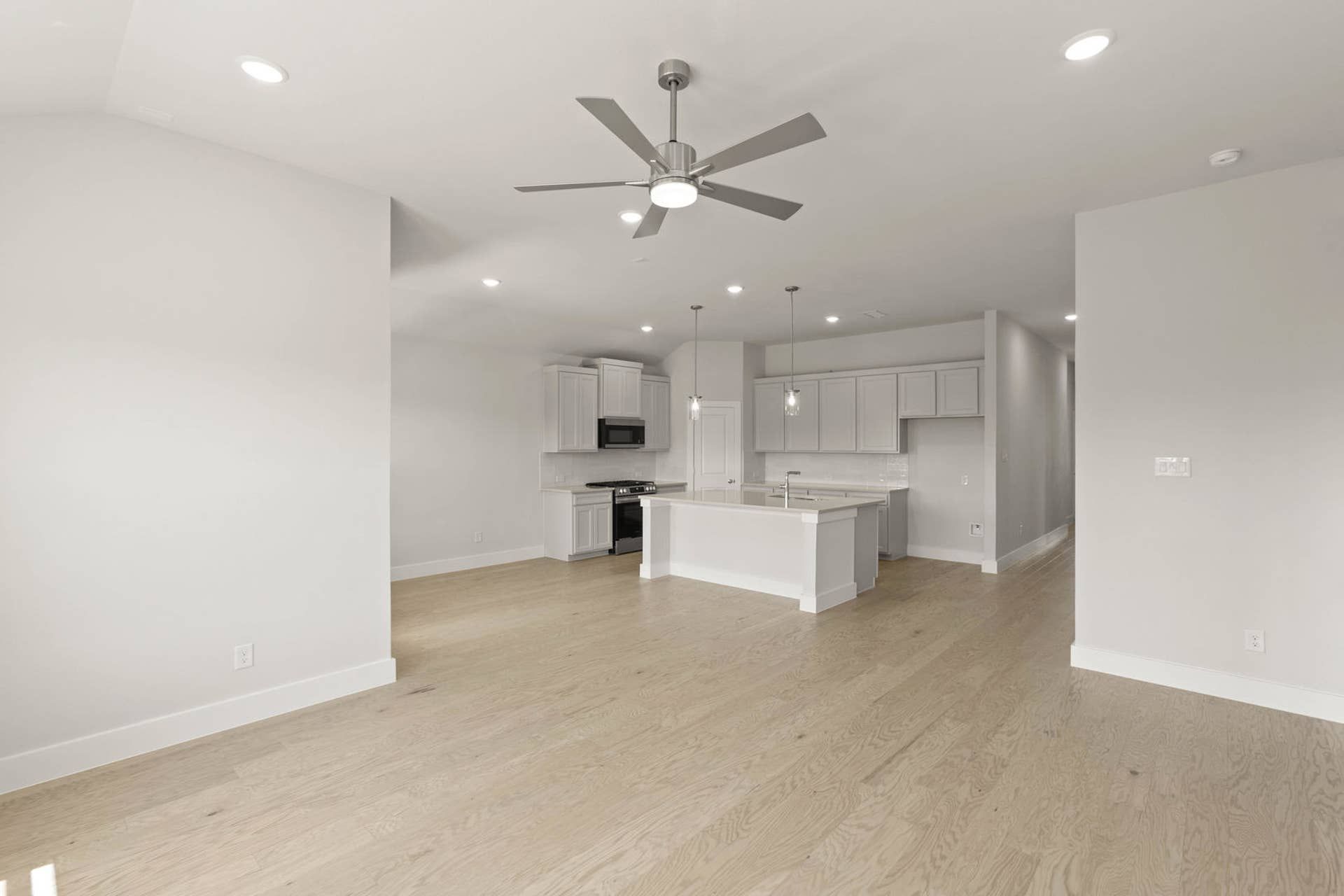 Spacious modern living room with open kitchen, hardwood floors, and ceiling fan.