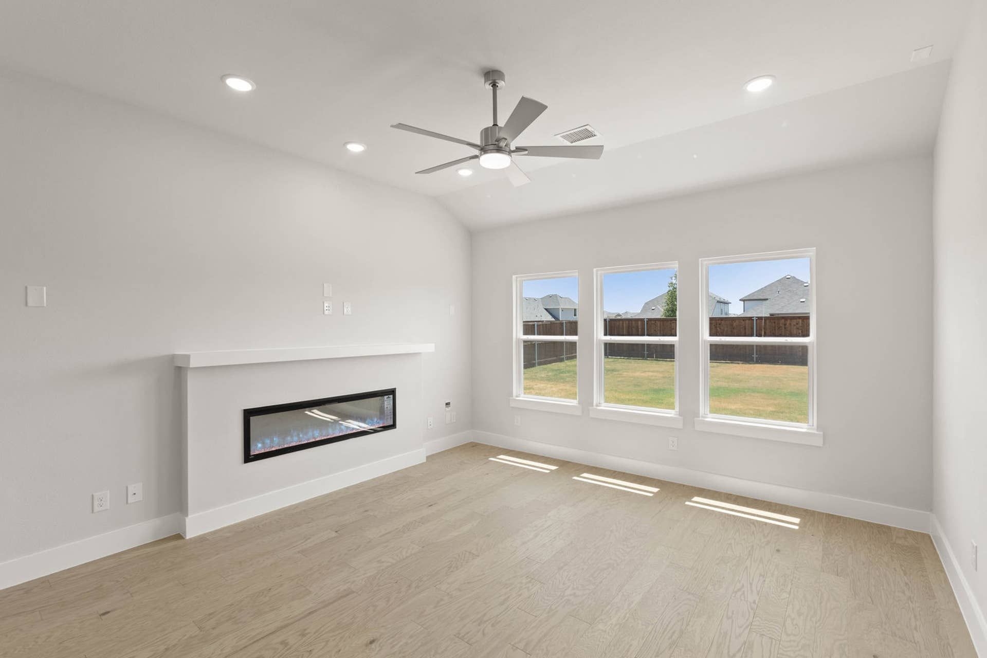 Modern living room with fireplace, large windows, and ceiling fan.